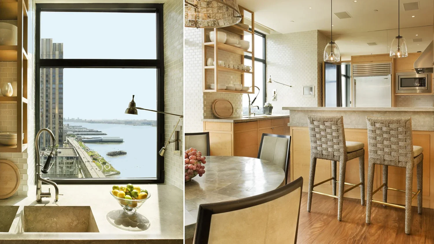 A kitchen with a view of a river through a large window. The kitchen has open shelving with dishes, a marble countertop, and a breakfast bar with woven chairs. There is a round dining table with chairs and a bowl of grapes and lemons. The space featu