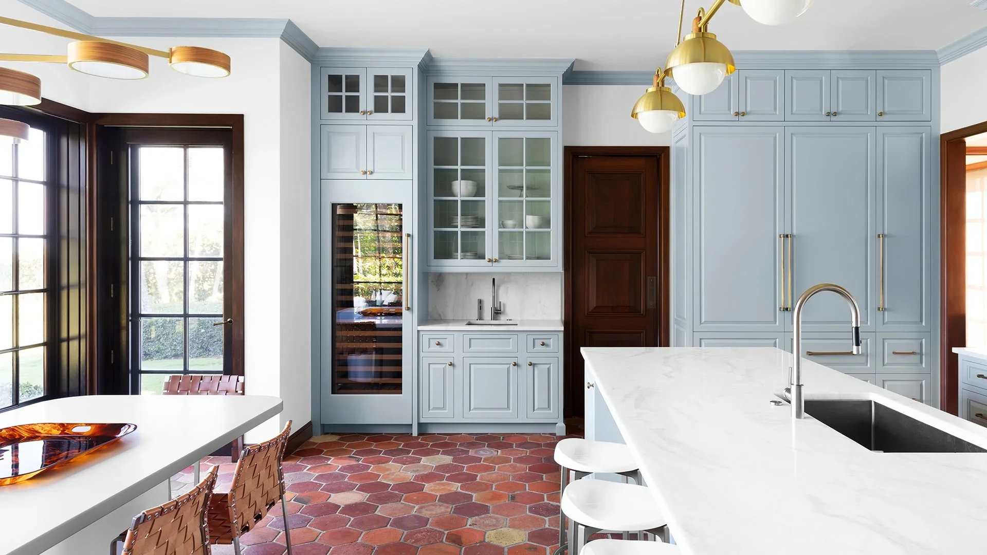 Modern kitchen with light blue cabinets, kitchen island with white marble countertop, built-in wine fridge, and a large window with black frames.