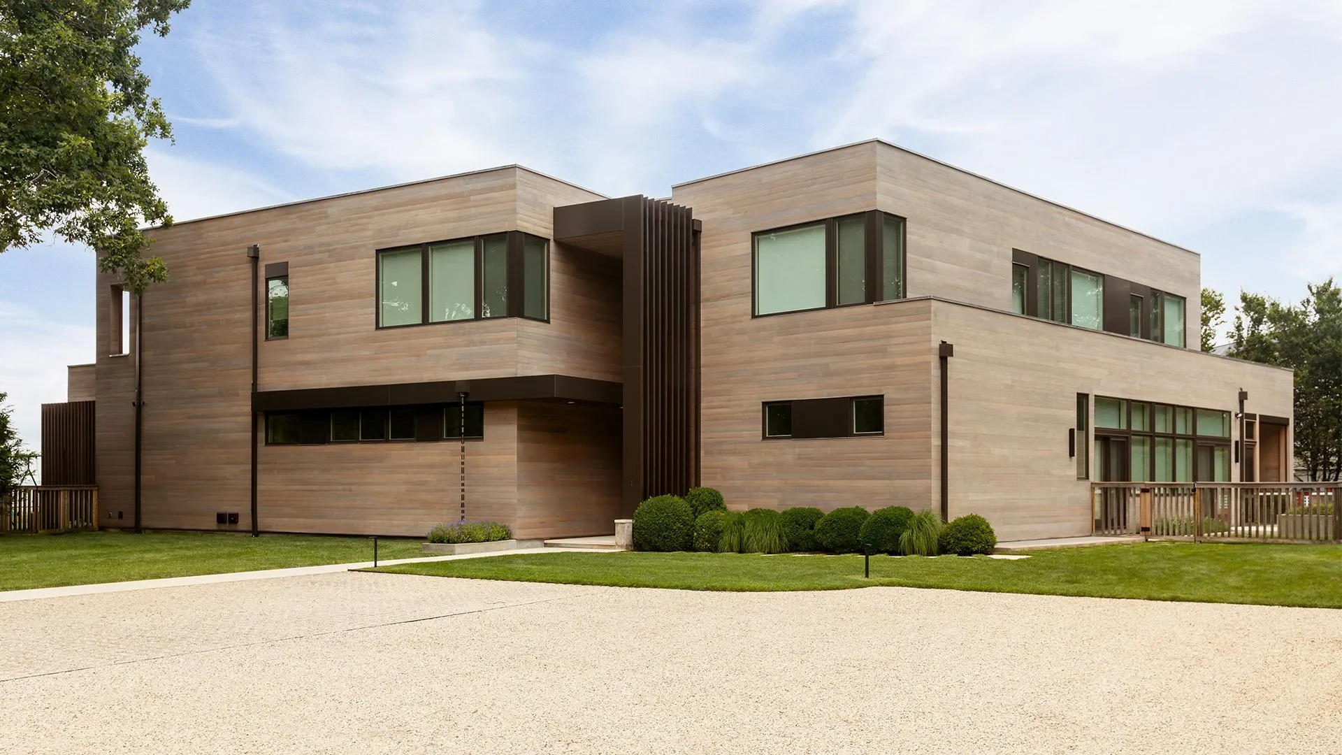 Modern two-story house with wooden exterior, large windows, and landscaped front yard