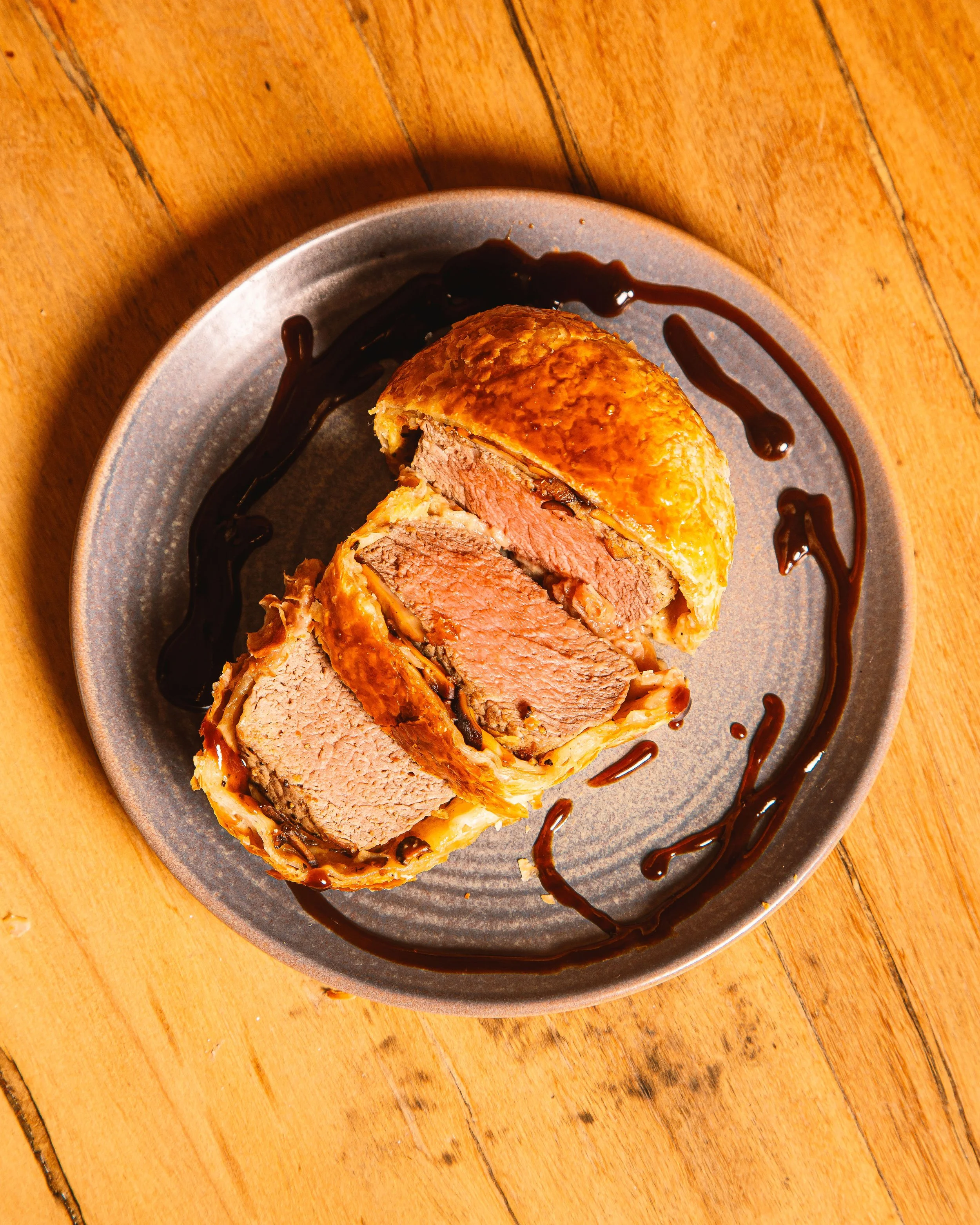 Beef Wellington with sliced beef, mushrooms, and flaky pastry, drizzled with balsamic glaze on a gray plate