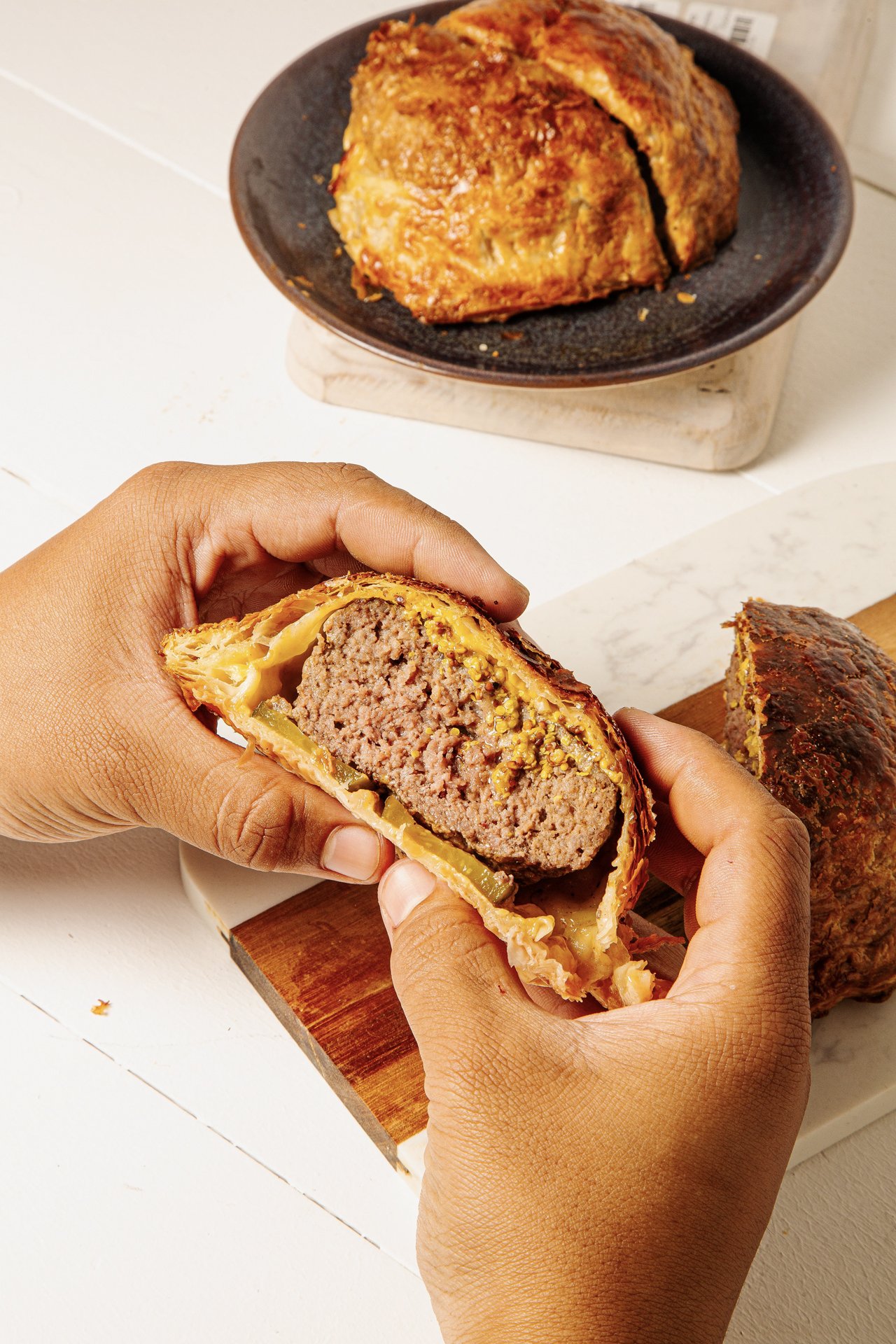Person holding a cooked meatloaf wrapped in pastry, showing a cross-section of the interior with meat and stuffing.