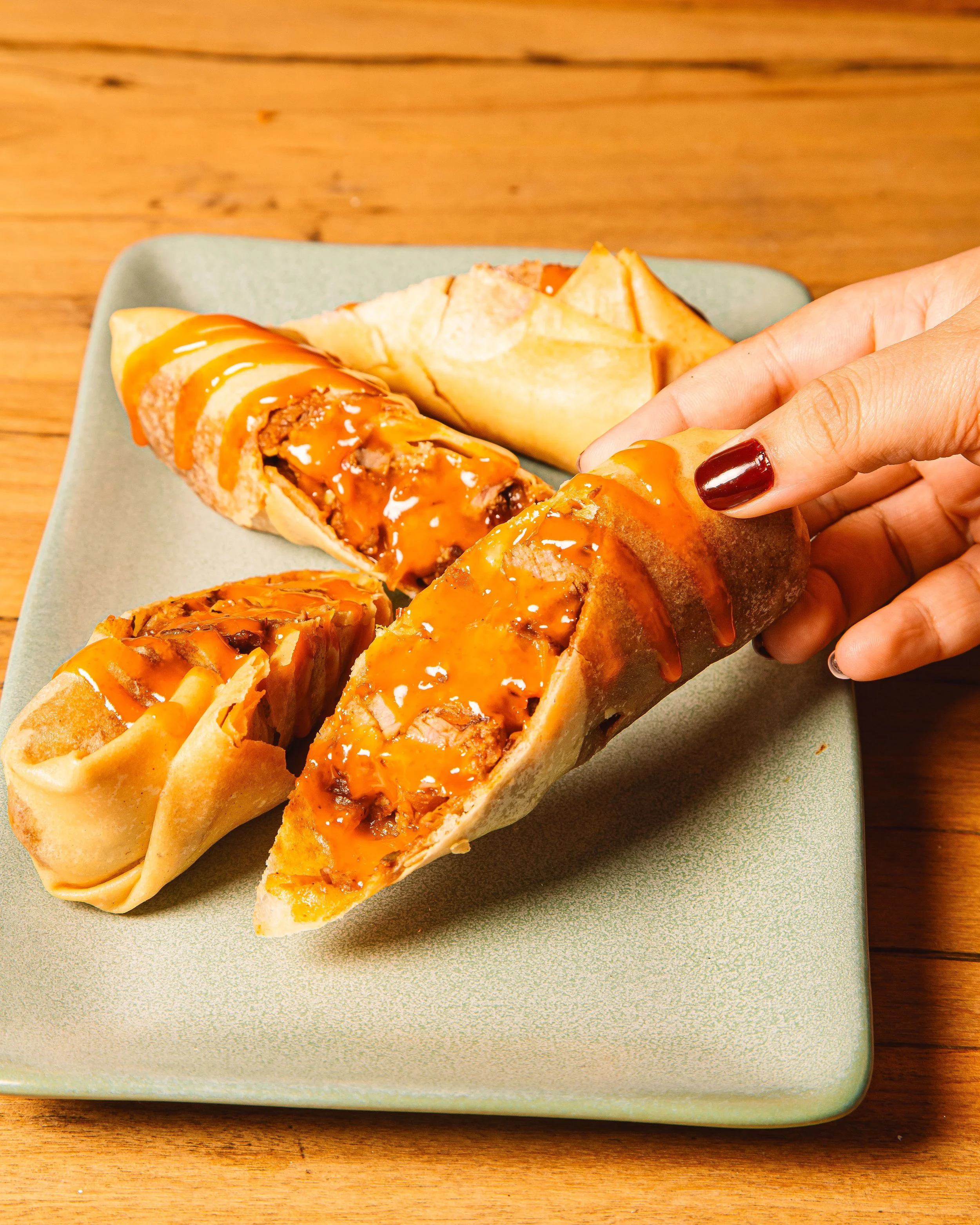 A hand holding a churro filled with caramel and chocolate with more churros on a green plate
