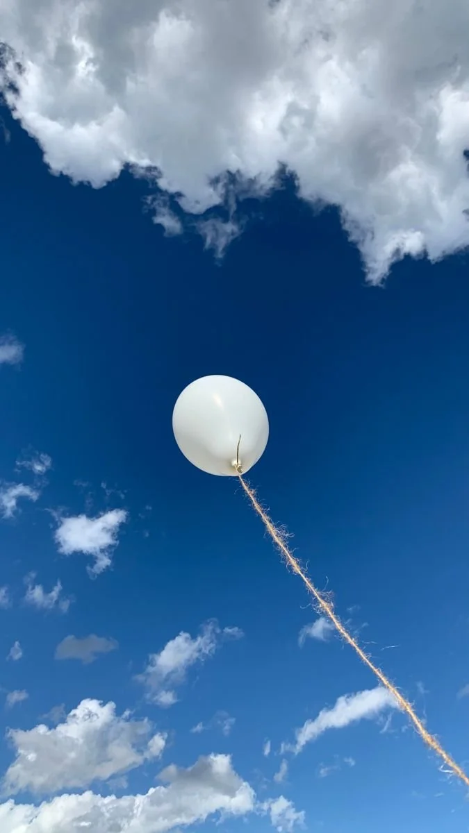 Un ballon blanc attaché à une corde flottant dans un ciel bleu avec des nuages blancs.