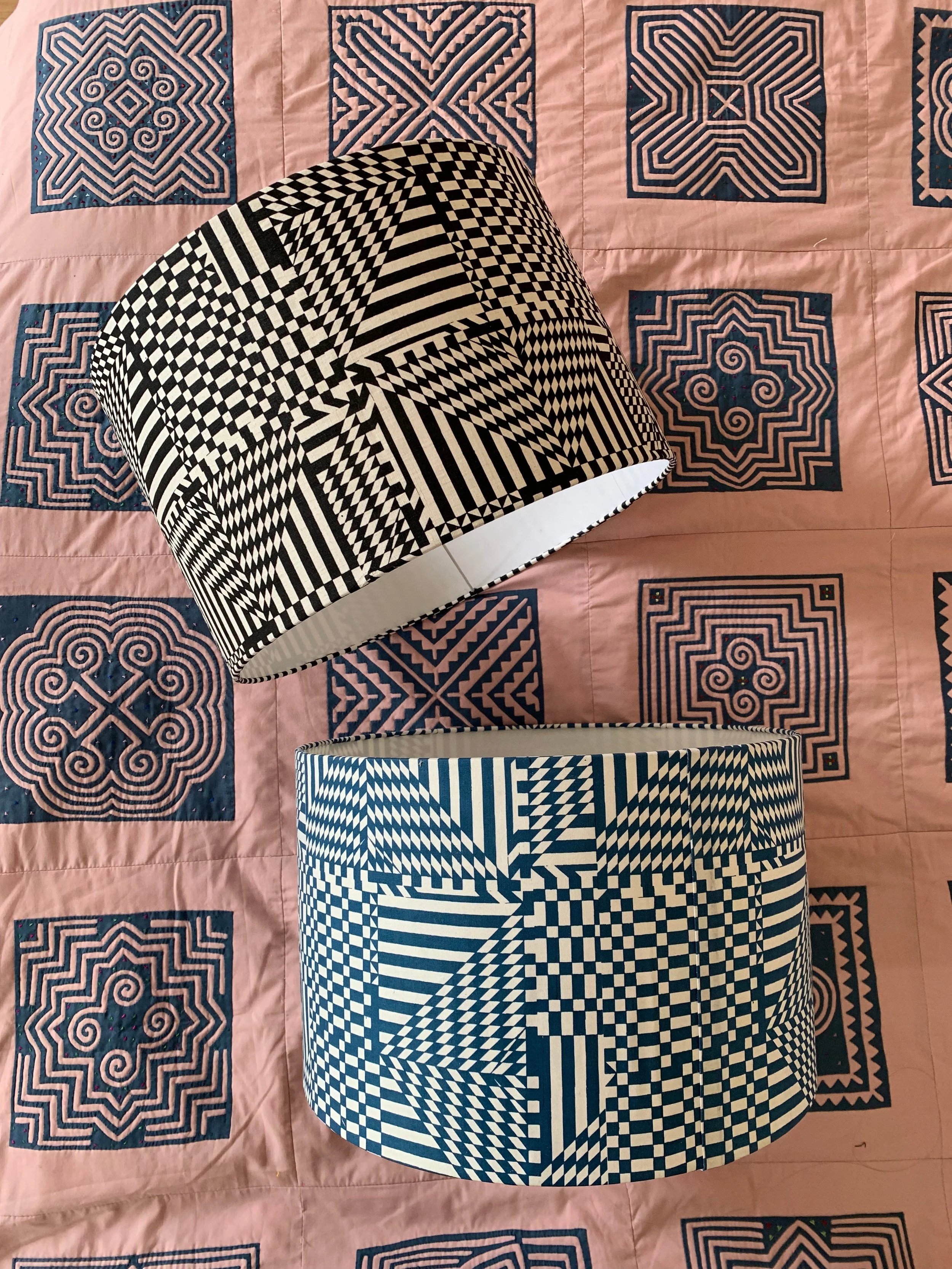Two lampshades with black and white geometric patterns, placed on a pink quilt with dark blue geometric quilt squares.
