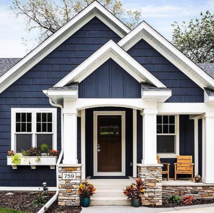 Front view of a dark blue house with white trim, a covered porch, stone accents, and a wooden bench.