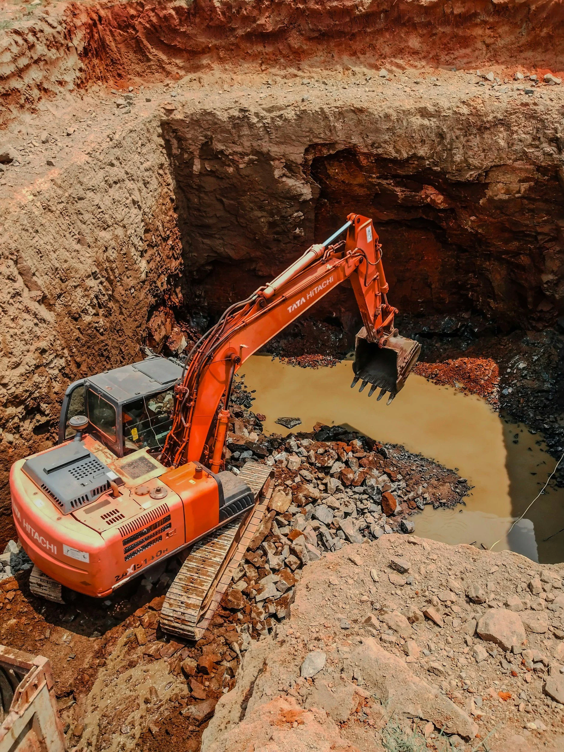 Kaivinkone kaivaa maata ja vettä kuopassa.