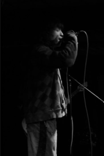 A person singing into a microphone on stage in a dark setting.