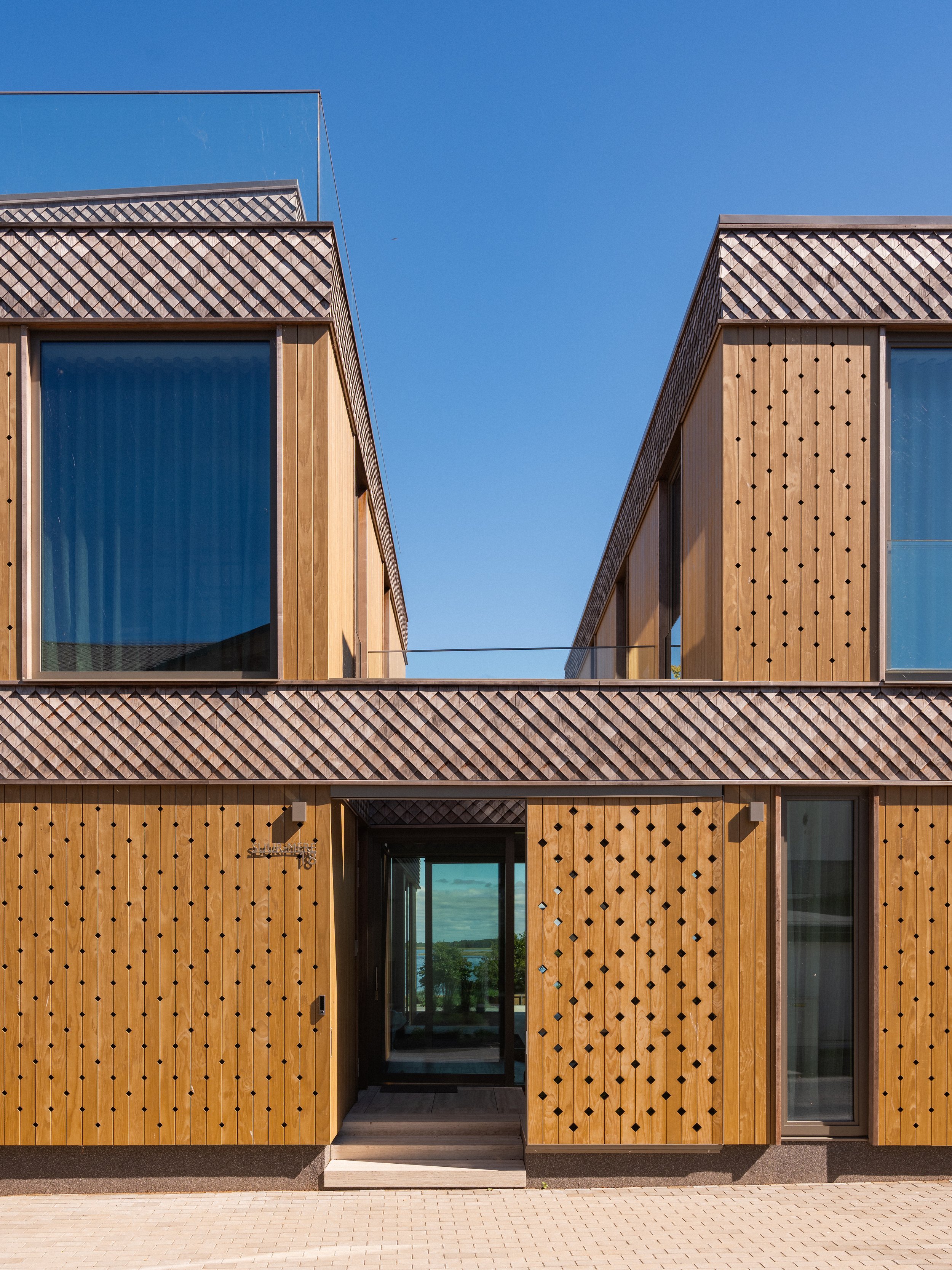 Modern wooden residential building with large glass windows and a blue sky.