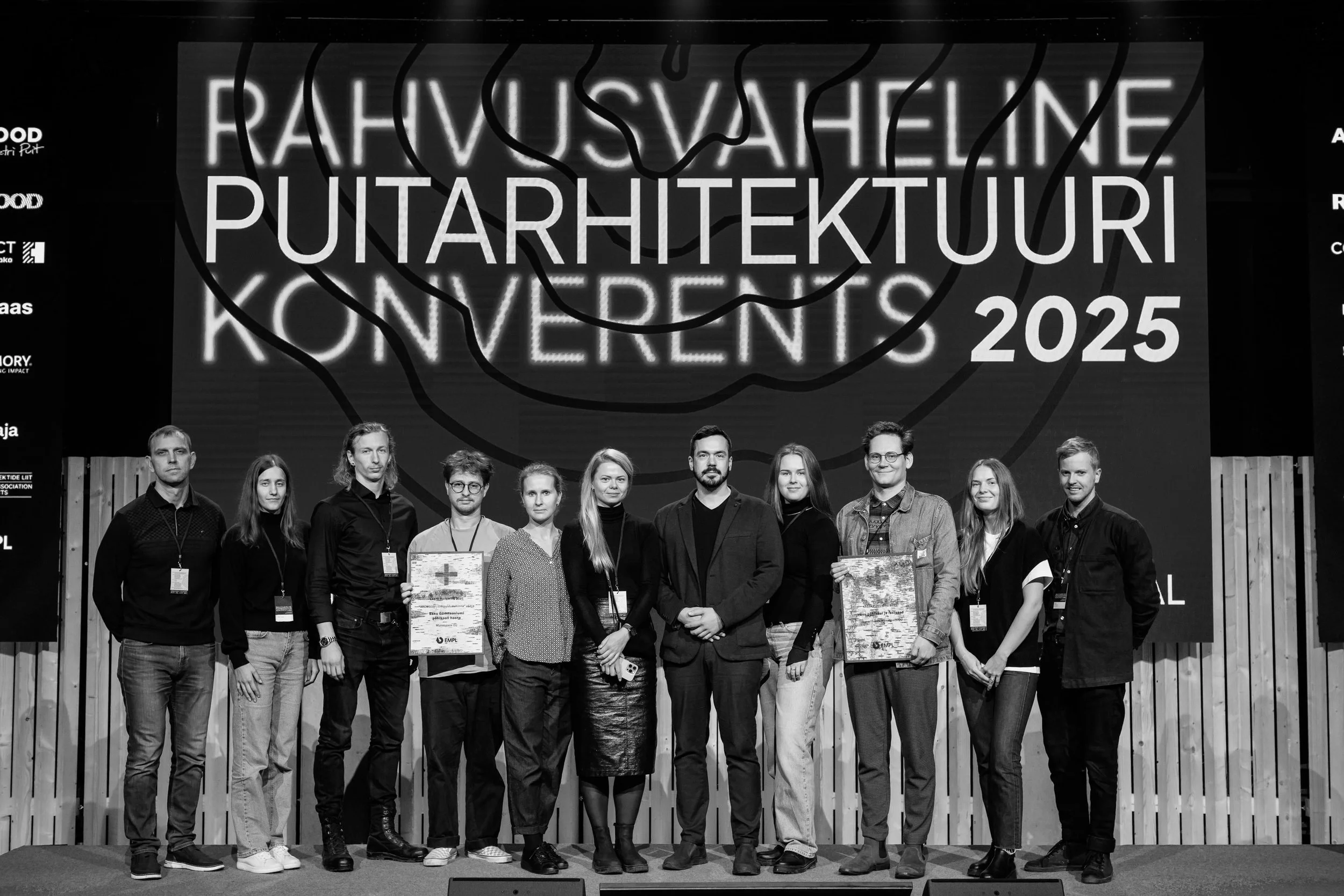 Group of eleven people standing on stage at the 2025 Architecture Conference, with a large screen behind them displaying the event name and year.