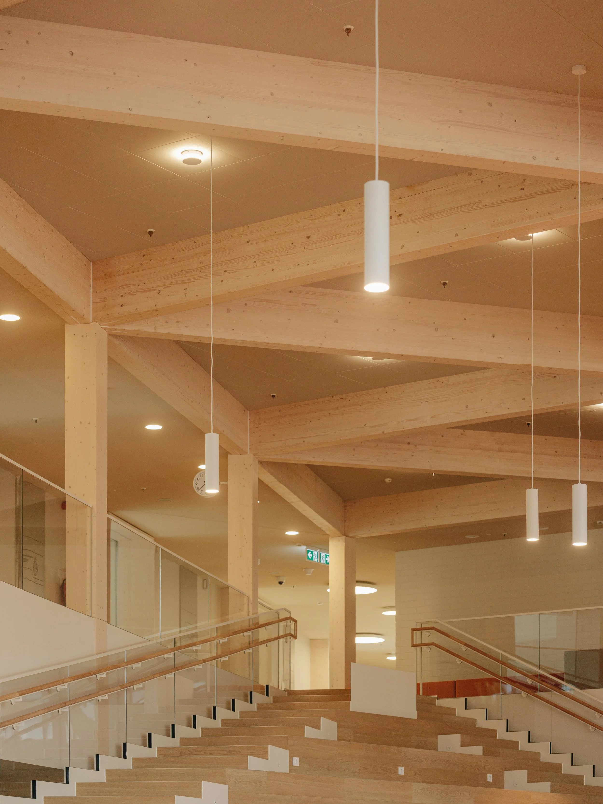 Modern interior space featuring wooden ceiling beams, pendant lights, and a staircase with glass railing.