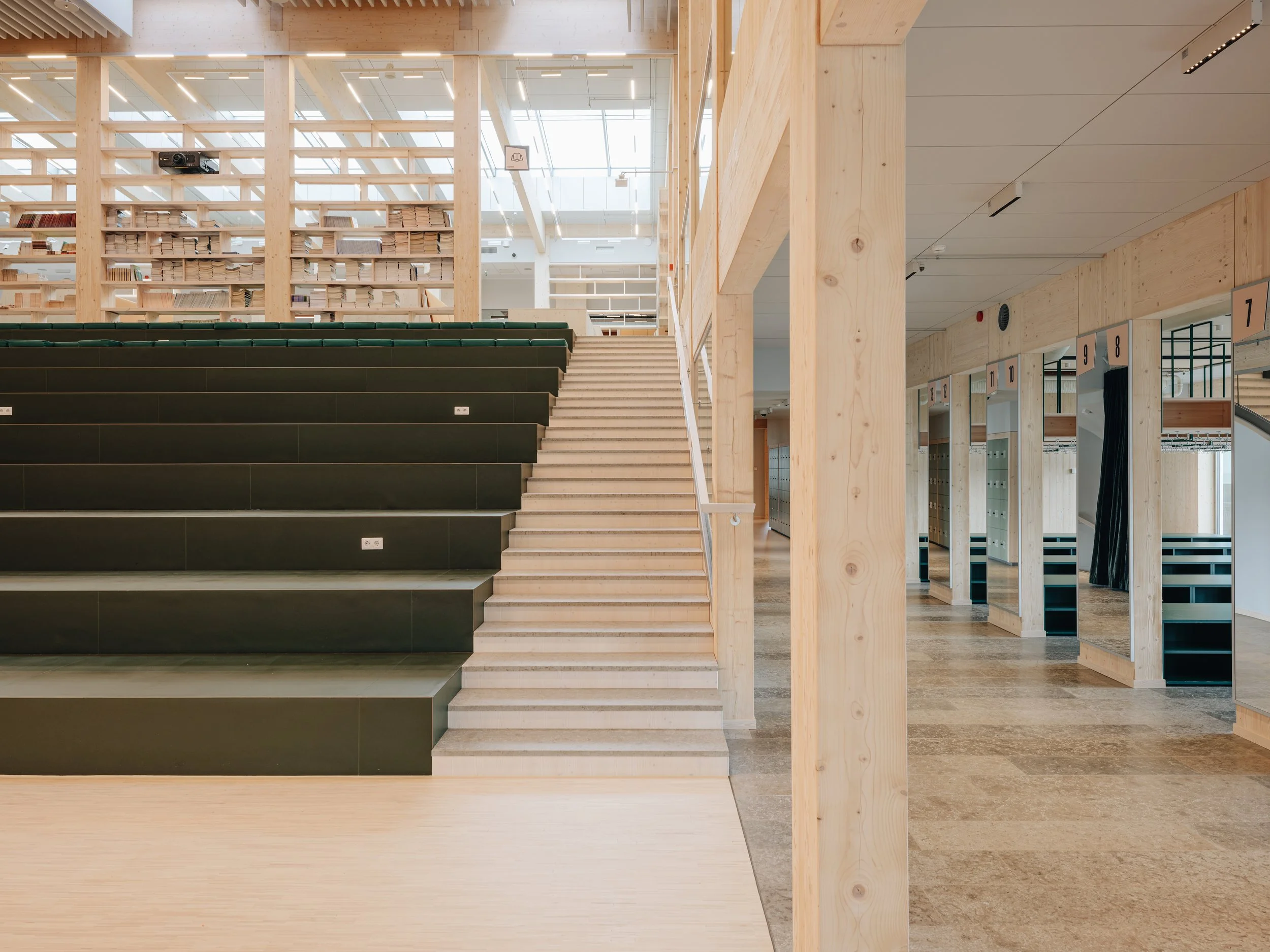 Inside a modern public library with a staircase, wooden columns, bookshelves, and library cubicles.