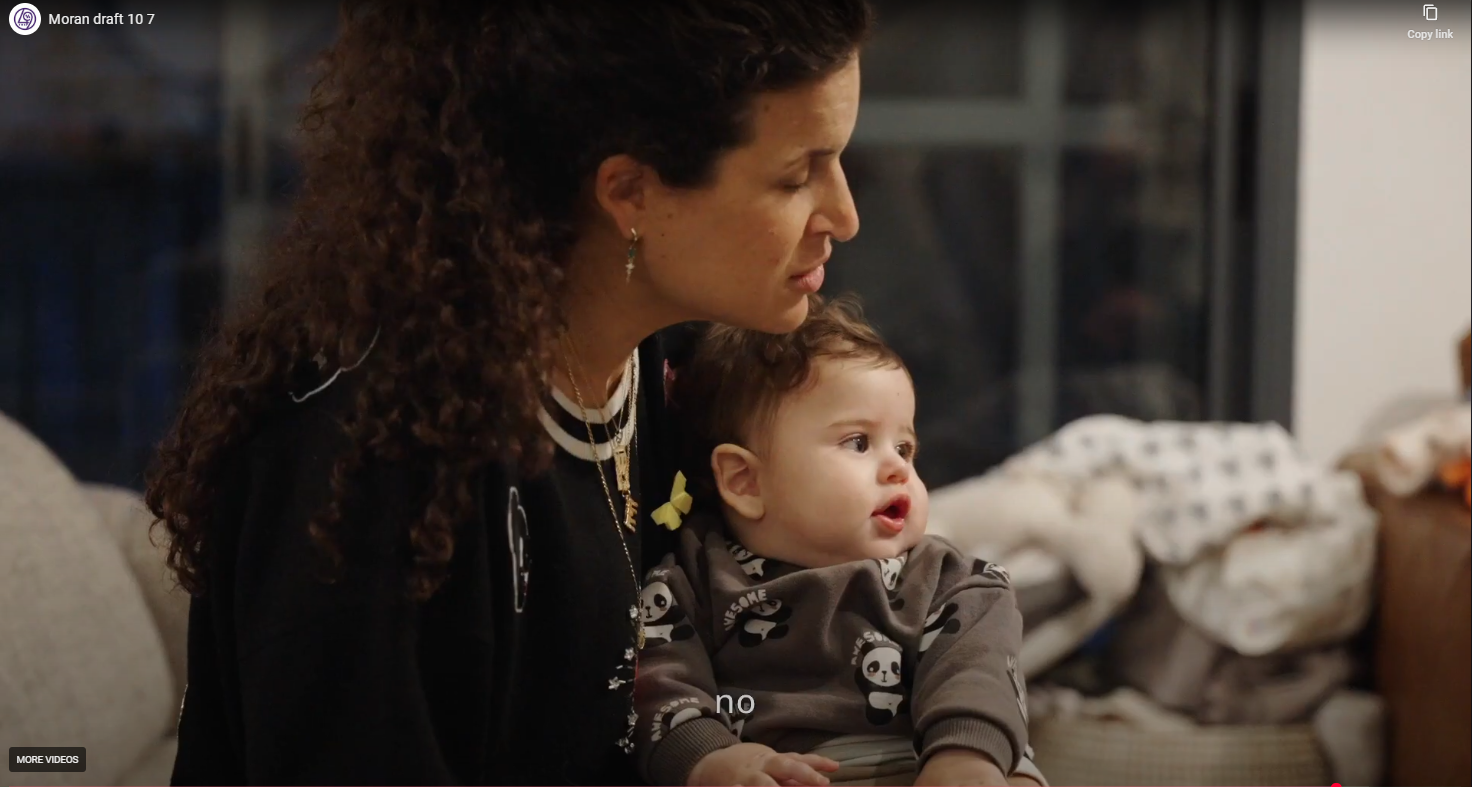 A woman with curly hair sitting on a beige couch, holding a young child with brown hair, wearing pajamas with panda prints, in a cozy living room with a fireplace and blankets in the background.