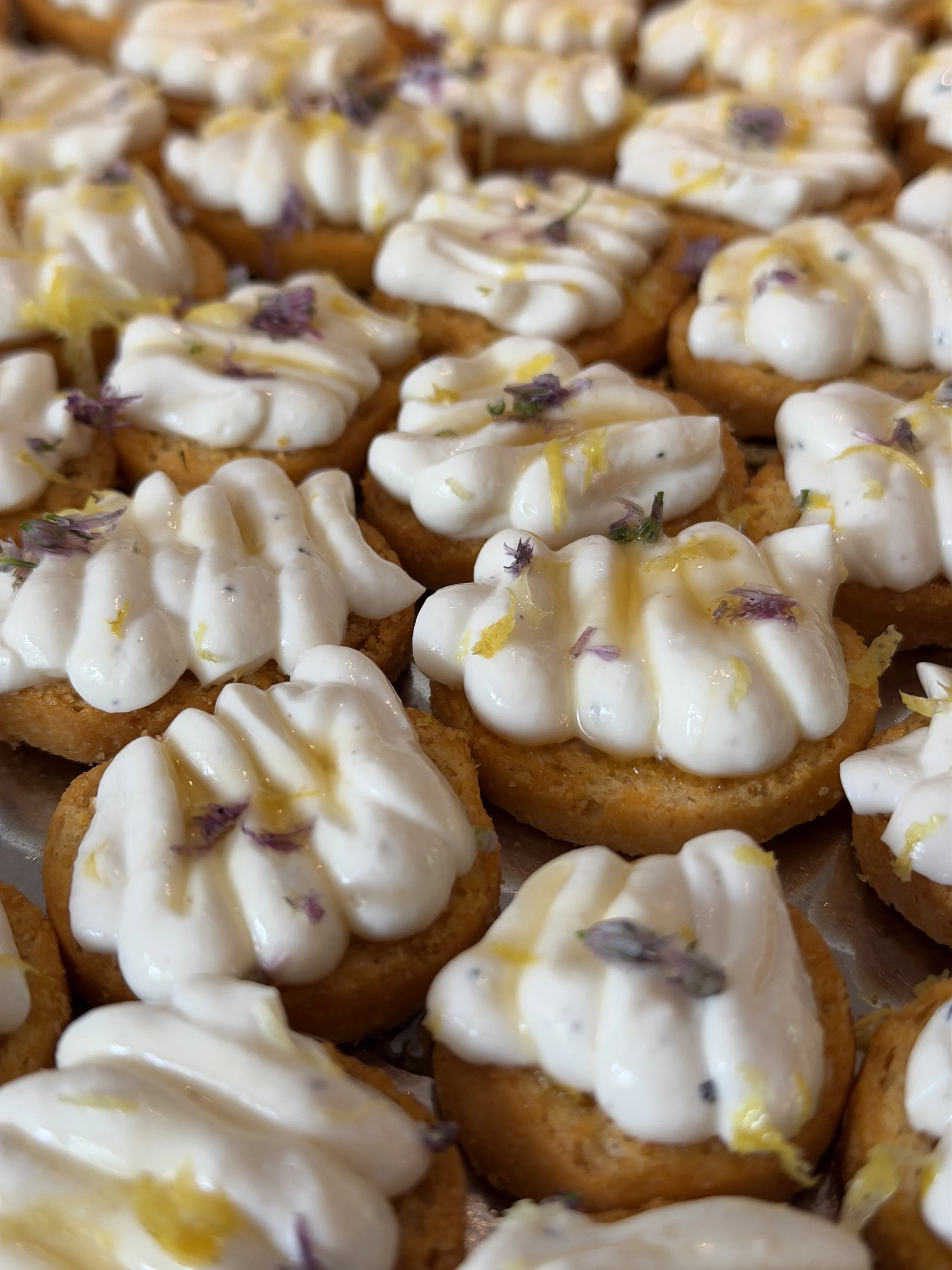 Close-up of small canapés topped with whipped cream, lemon zest, and edible flowers.