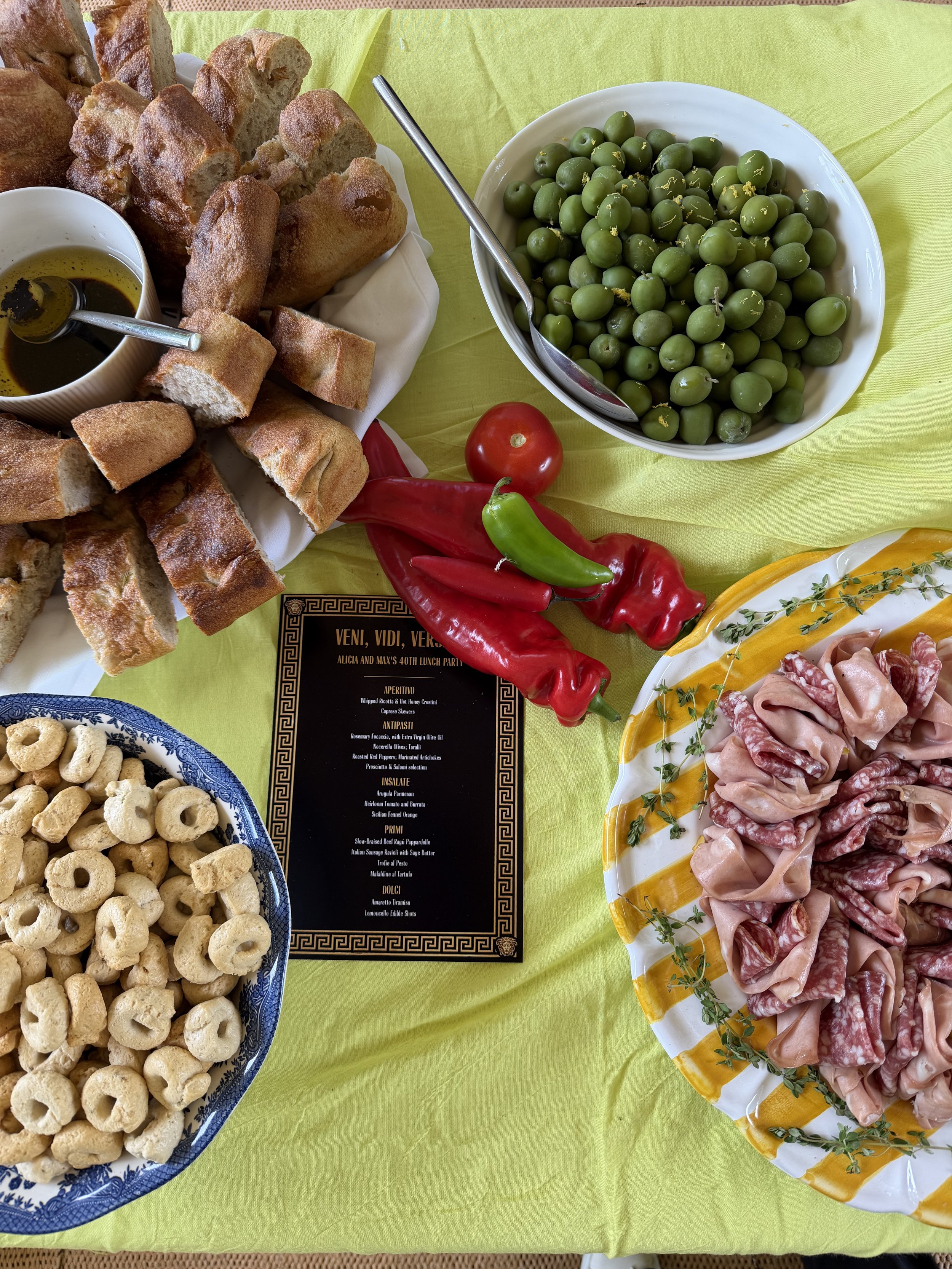 A table with a spread of Italian antipasto and appetizers, including bread, olives, cured meats, and cheese, with a menu in the center.