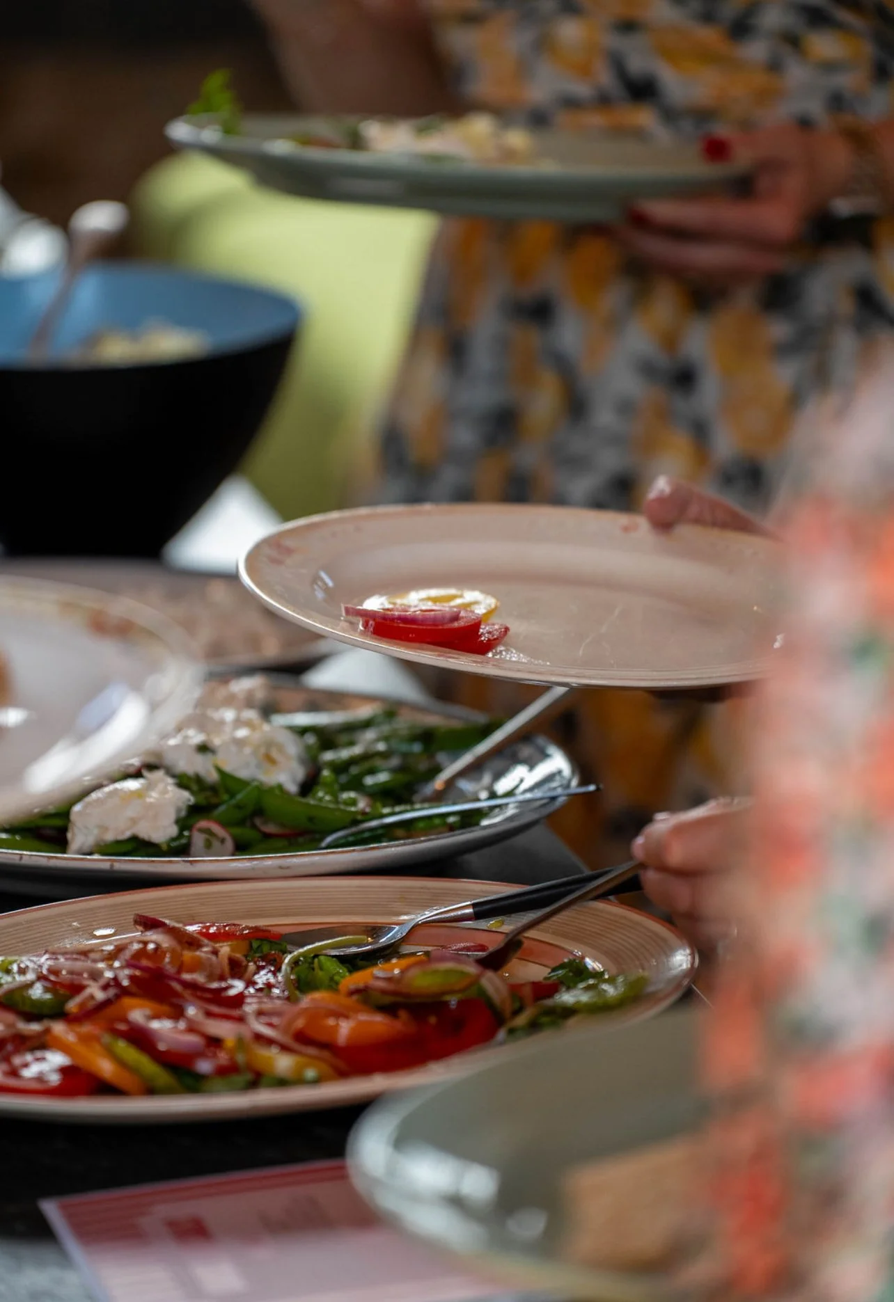 Close-up of plates with colorful salads and sliced vegetables on a table at a buffet or shared meal.