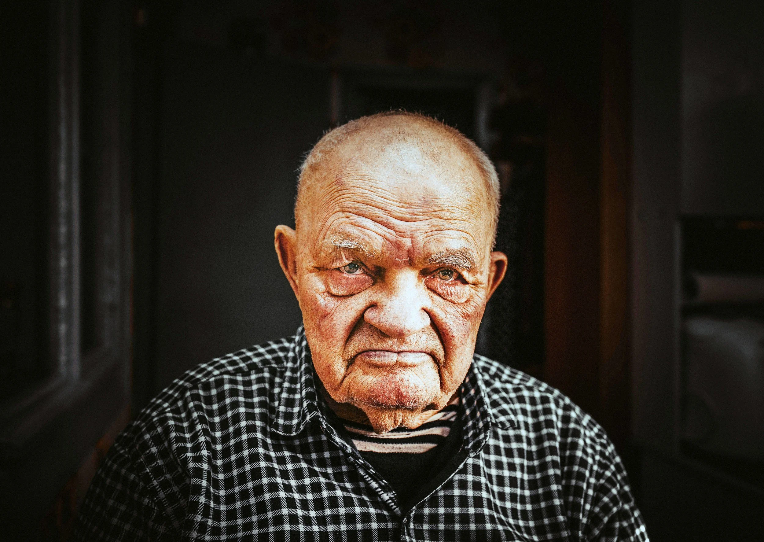 Close-up portrait of an elderly man with a serious expression, representing the emotional complexity of caring for an aging parent