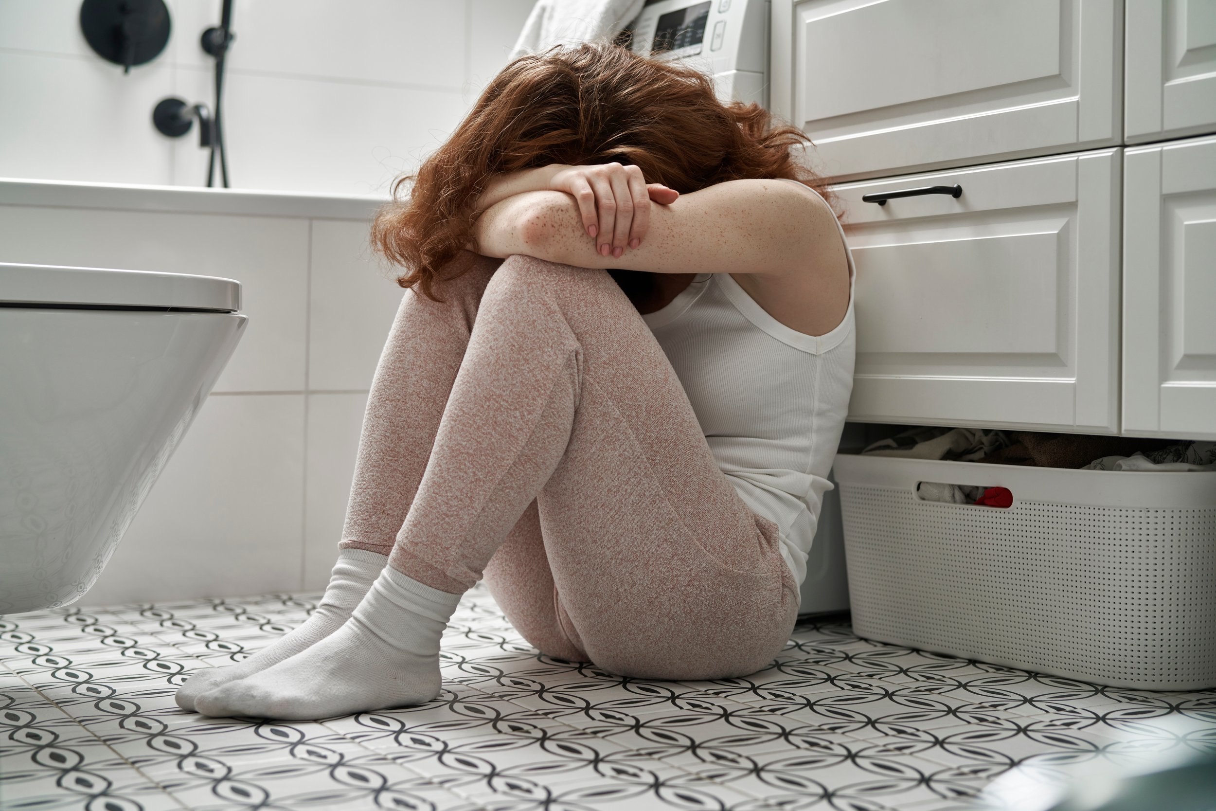 A woman sitting on the bathroom floor struggling to process past trauma.