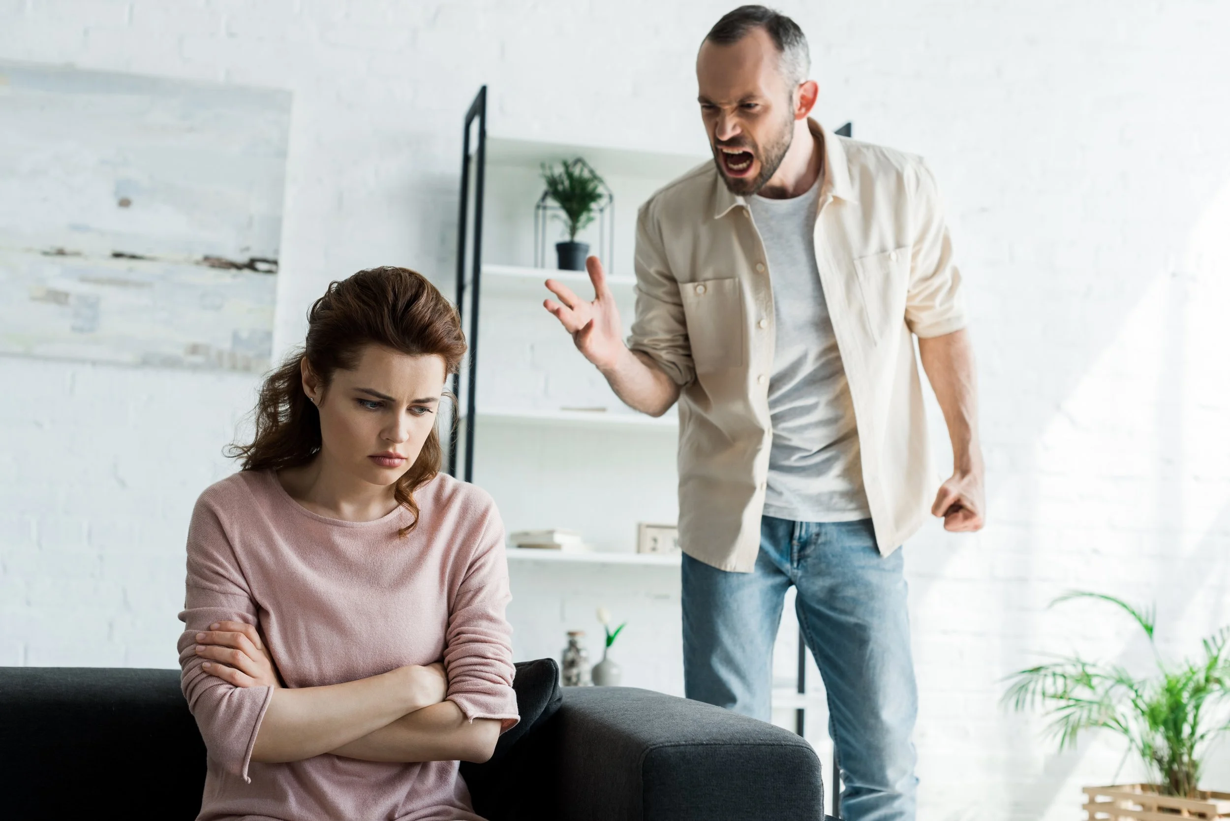 A man angrily arguing with a woman who looks upset and crossed her arms in a living room.