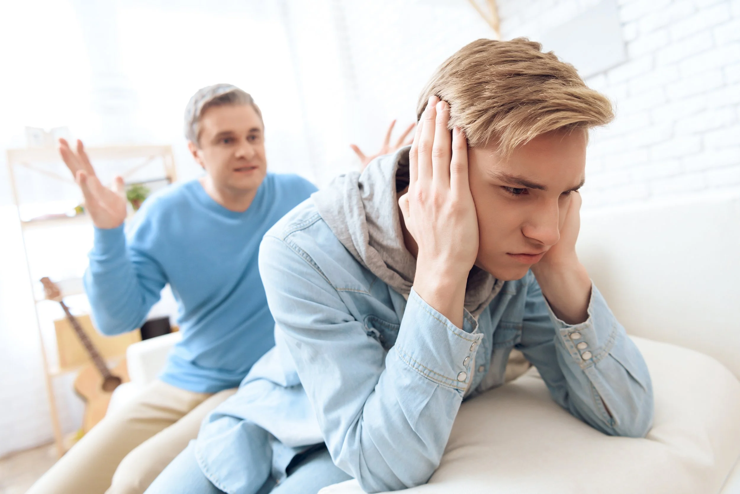 Young man upset, covering his ears, with an angry person yelling at him in the background.
