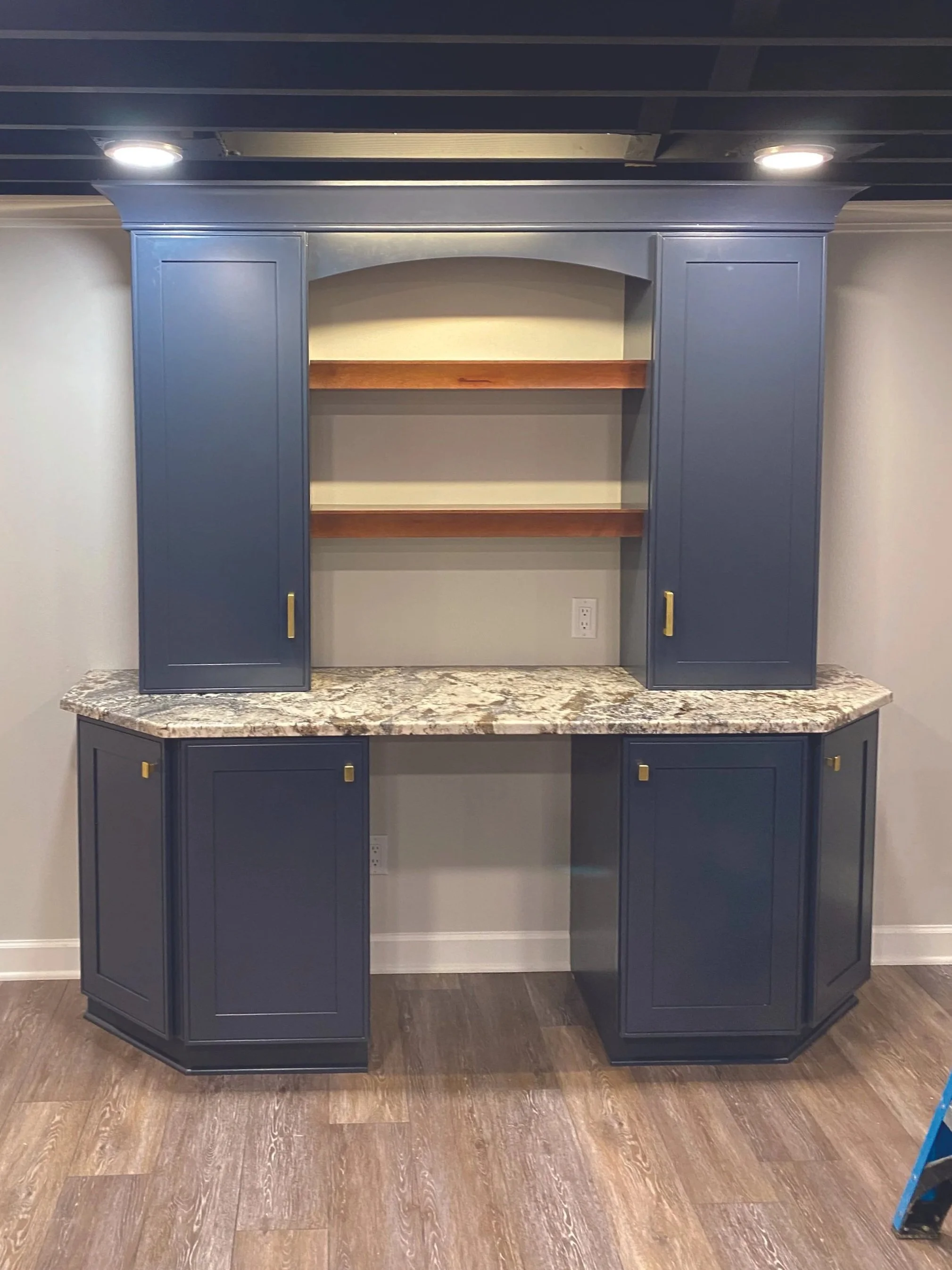 Blue kitchen cabinet with marble countertop, open shelving, and closed cabinets below, set against a light-colored wall.