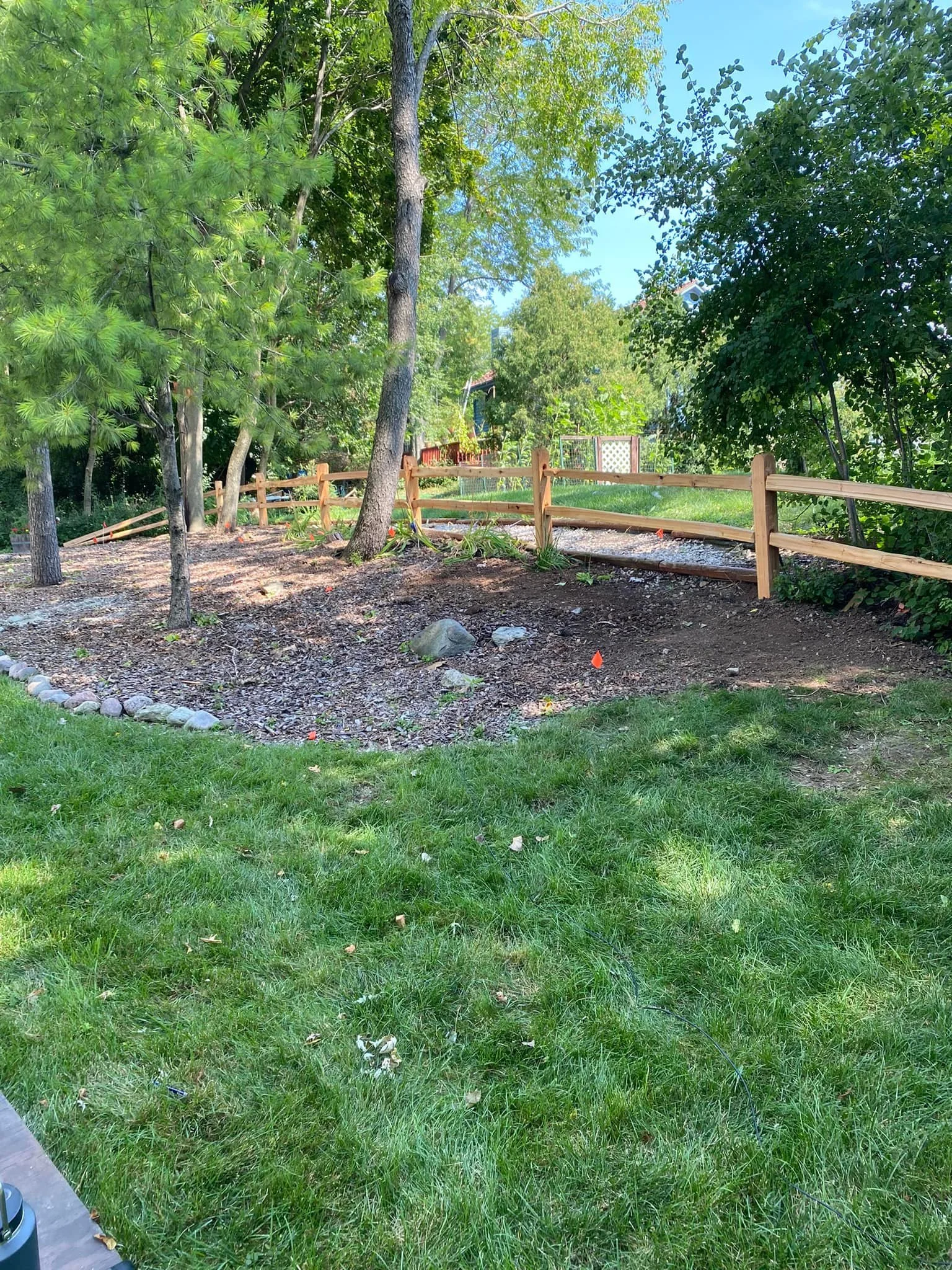 Backyard with green grass, trees, and a wooden fence under a sunny sky, with some construction or landscaping work in progress.