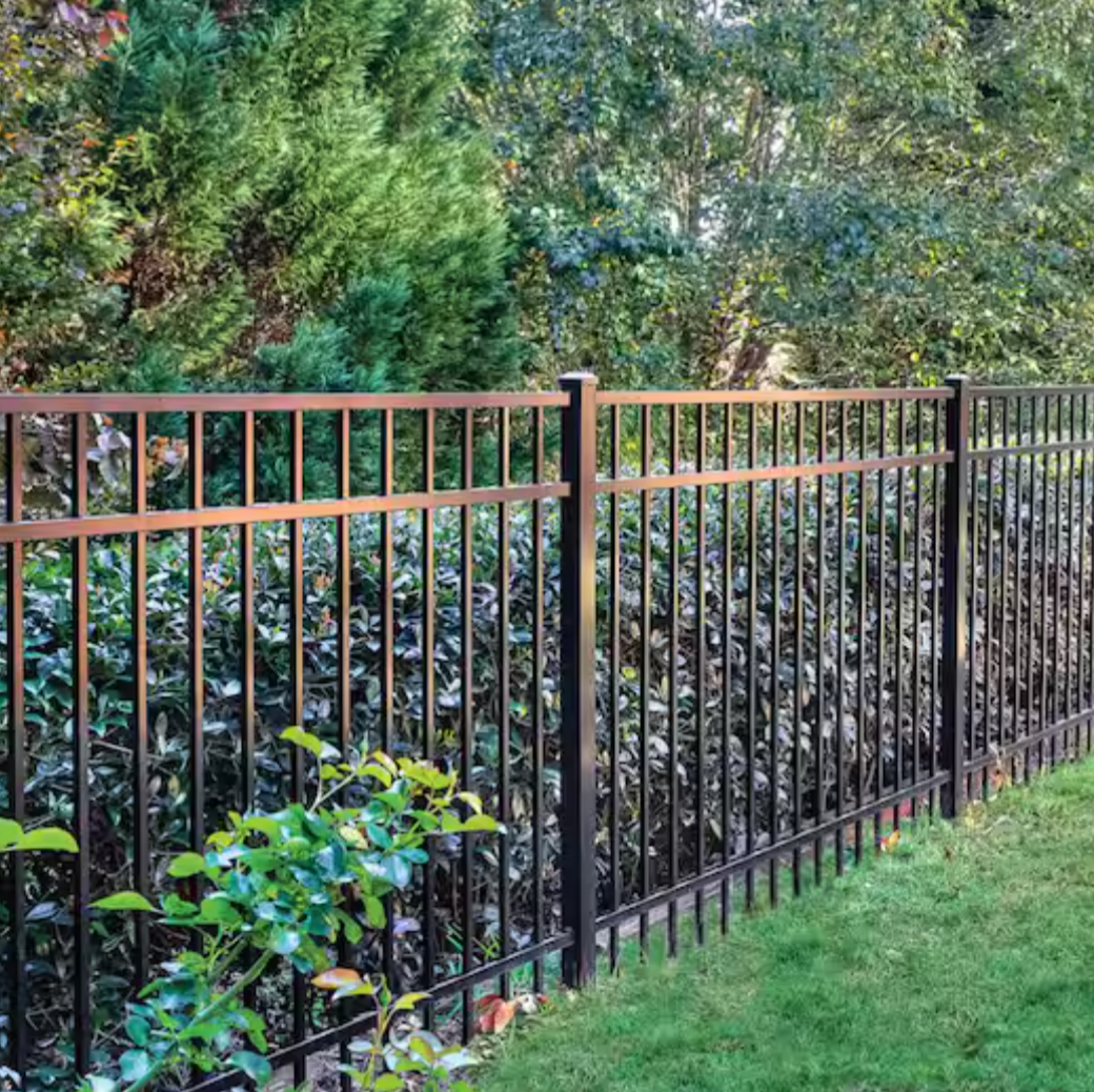 A black metal aluminum fence separates a well-maintained grassy yard from a lush garden with green leafy bushes and trees.