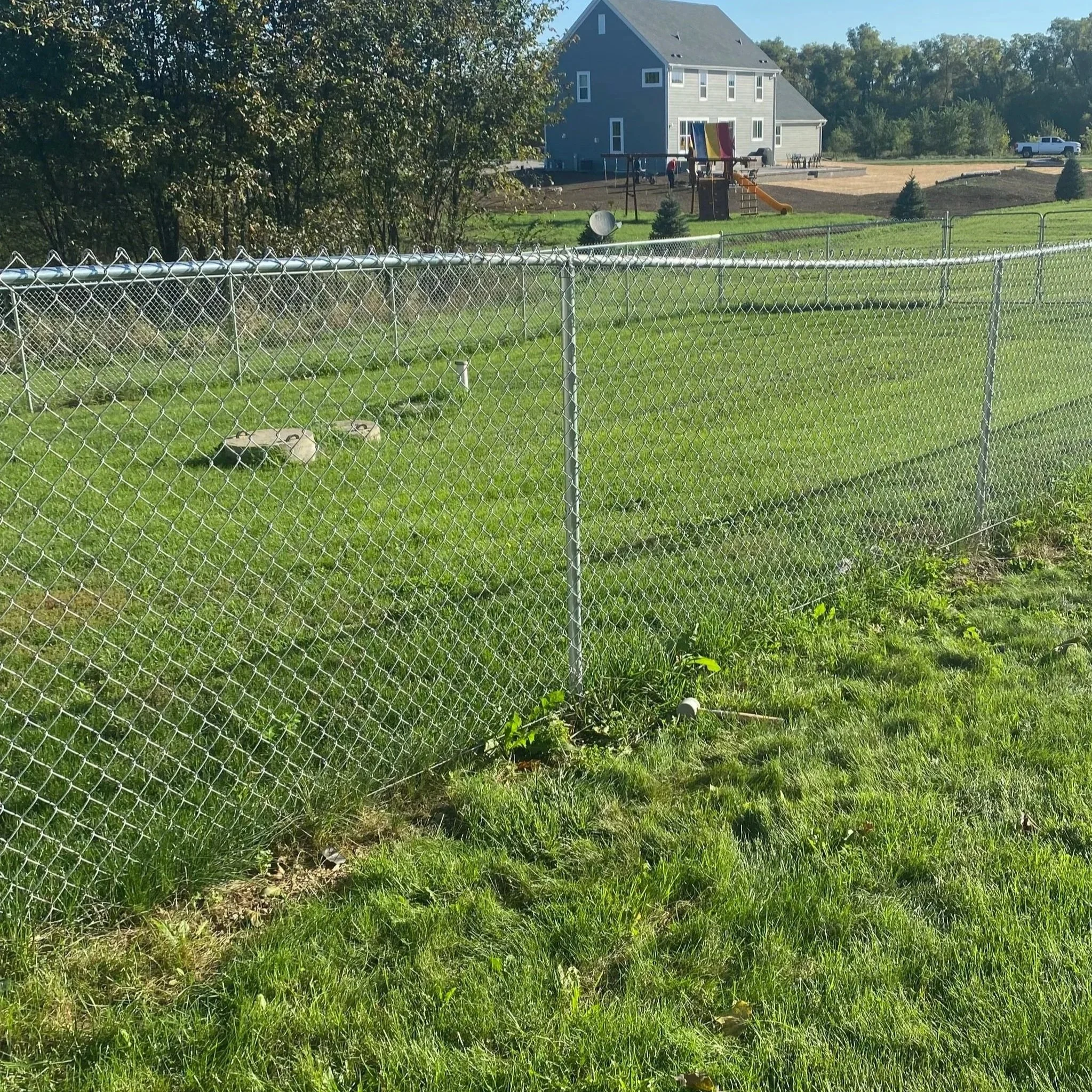 A chain-link fence borders a grassy backyard with a house and playground in the background.