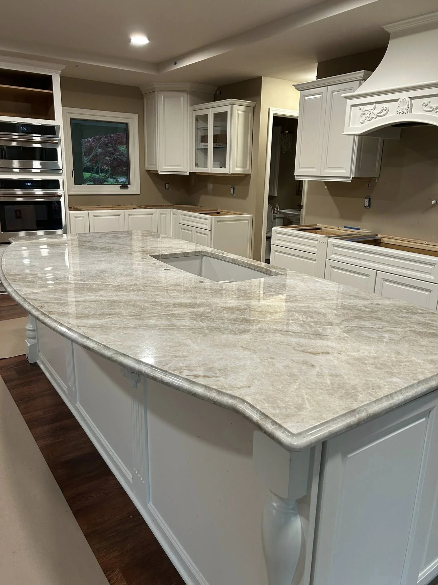 Newly renovated kitchen with white cabinets, beige walls, and a large marble island with a built-in sink, hardwood floors, and an oven unit.