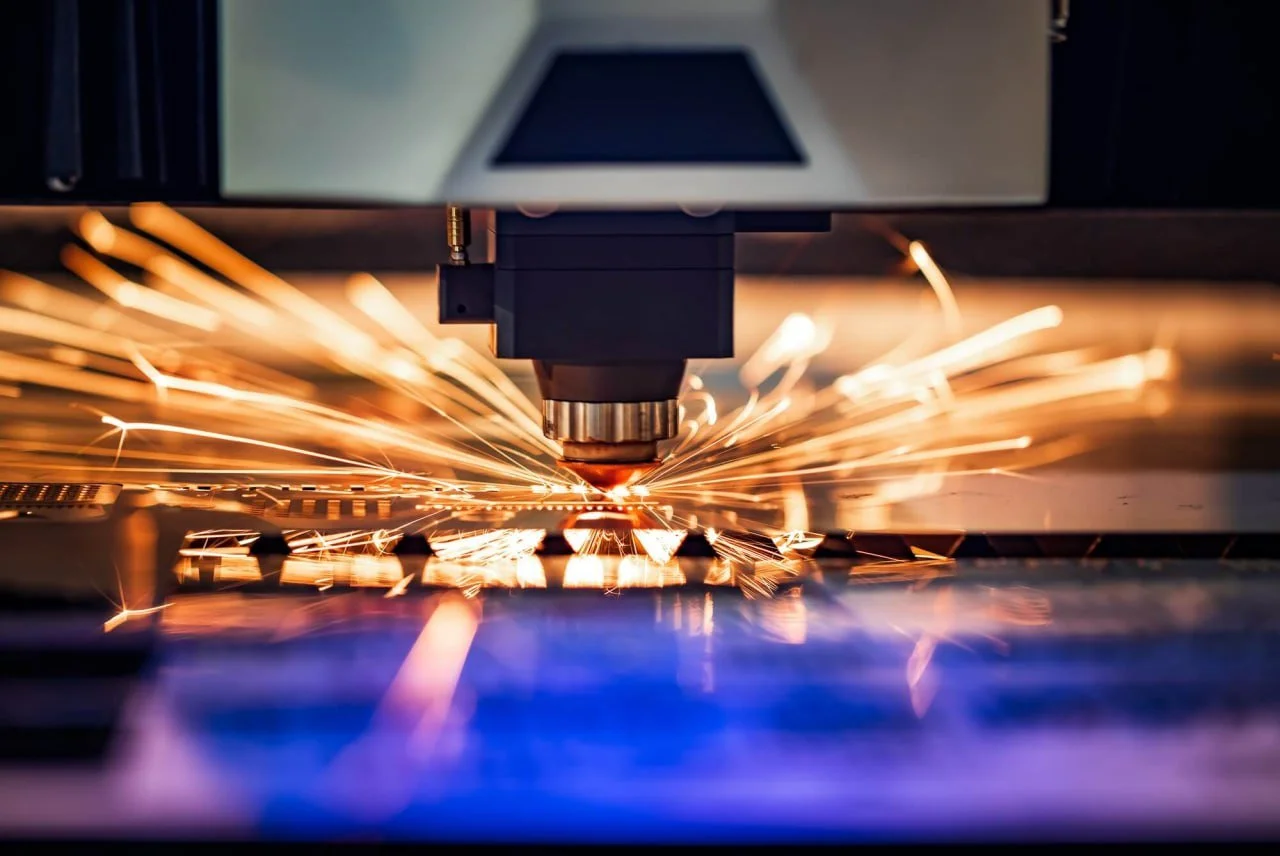 Close-up of a laser cutting machine in action with sparks flying as it cuts through metal.