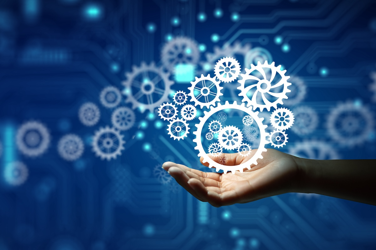 A hand holding a virtual futuristic display of interconnected white gears against a blue technological background.