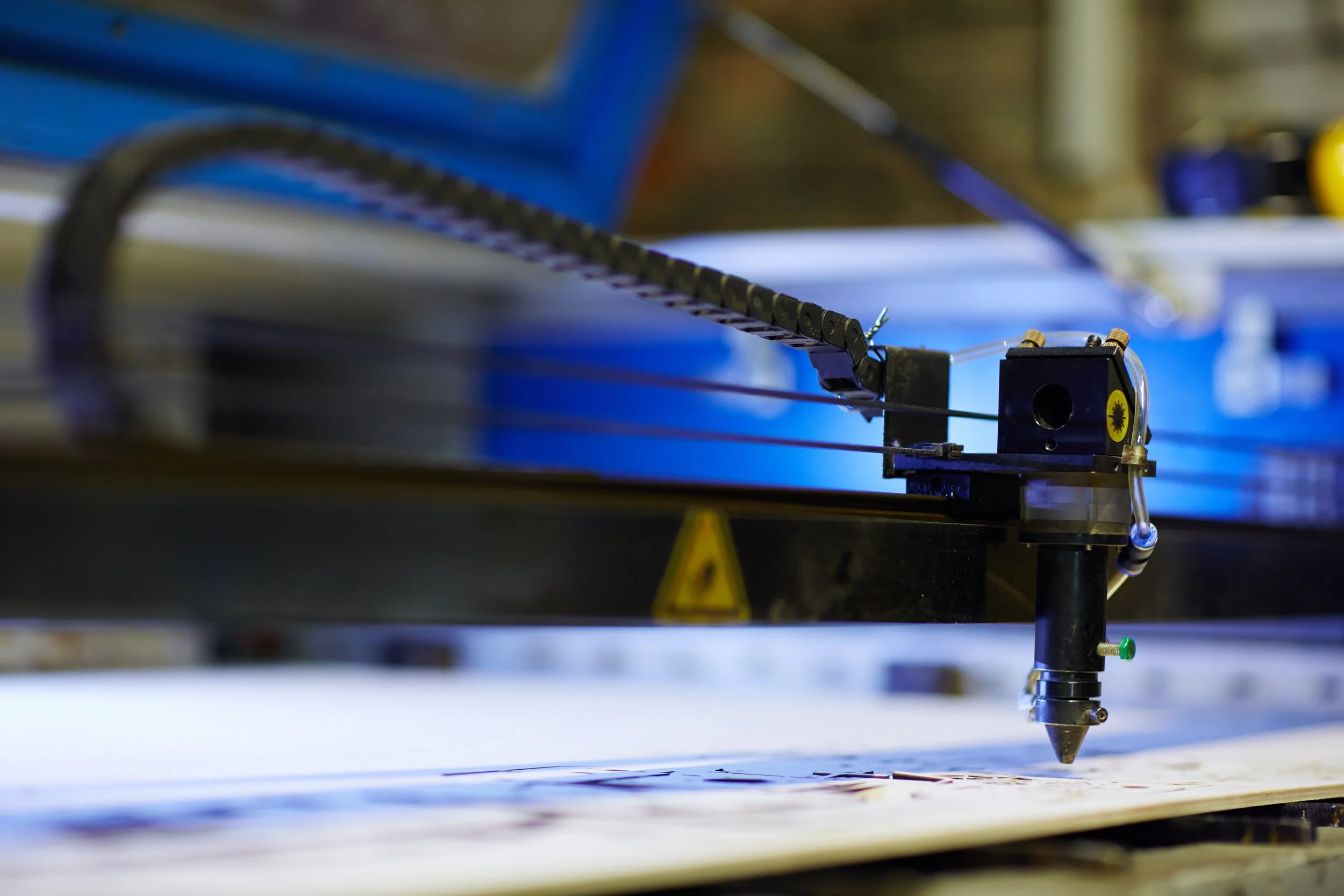 A close-up of a laser cutter or engraver with a laser beam focused on a piece of material, showing the machinery and tools used for precise cutting or engraving.