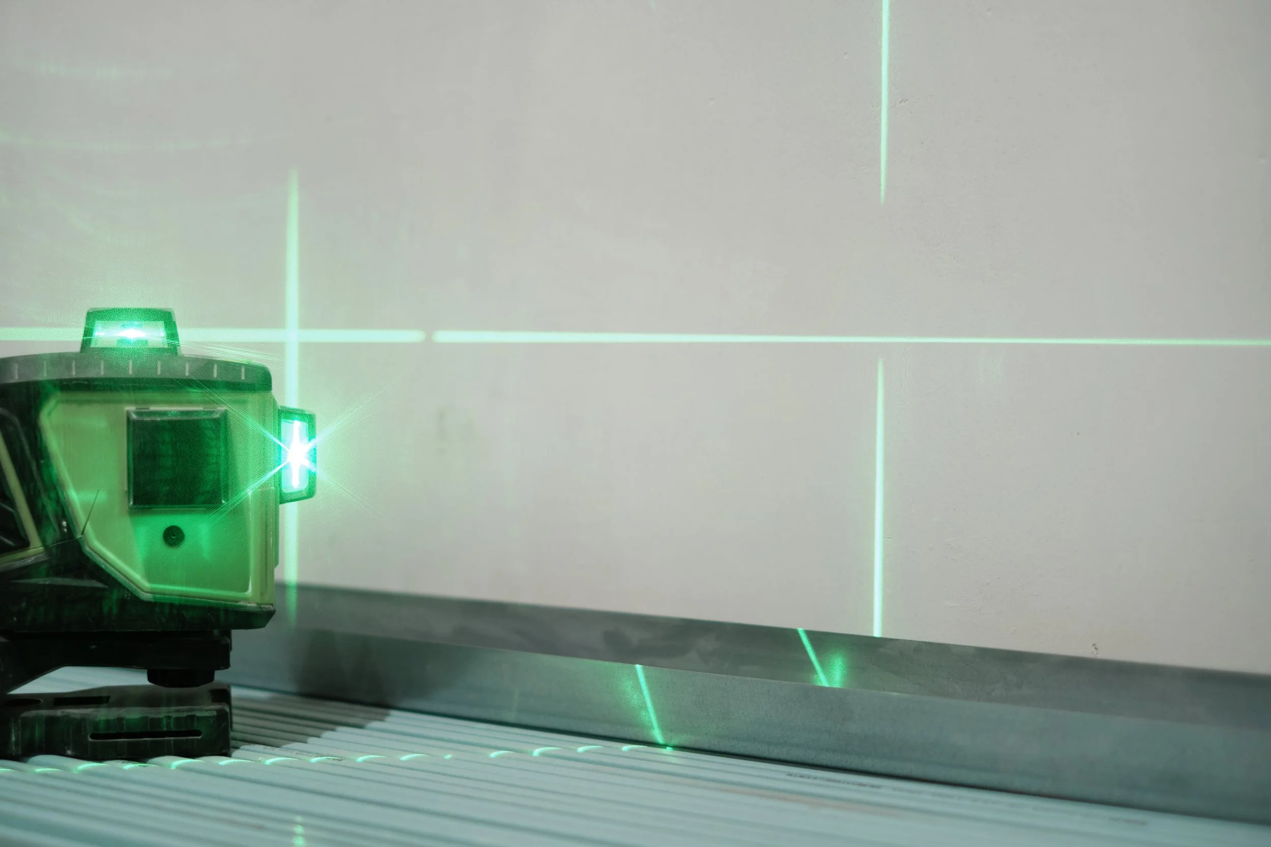 A laser level projecting green crosshairs on a wall, sitting on a striped surface.