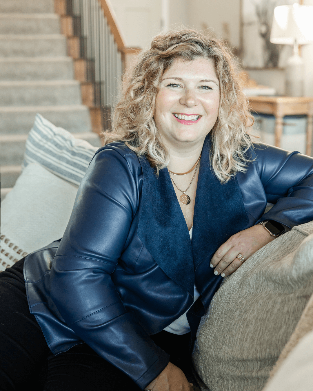 Lauren Cockerell, business leader and marketing advisor, sits on a sofa in a modern living room, smiling warmly in a blue jacket.