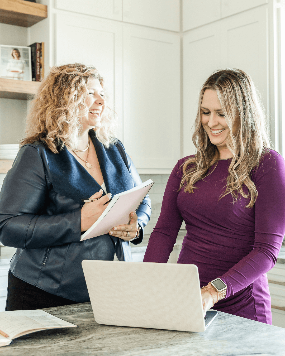 Lauren Cockerell, founder and communications strategist, laughs with a colleague while reviewing marketing plans on a laptop in a bright, open workspace.