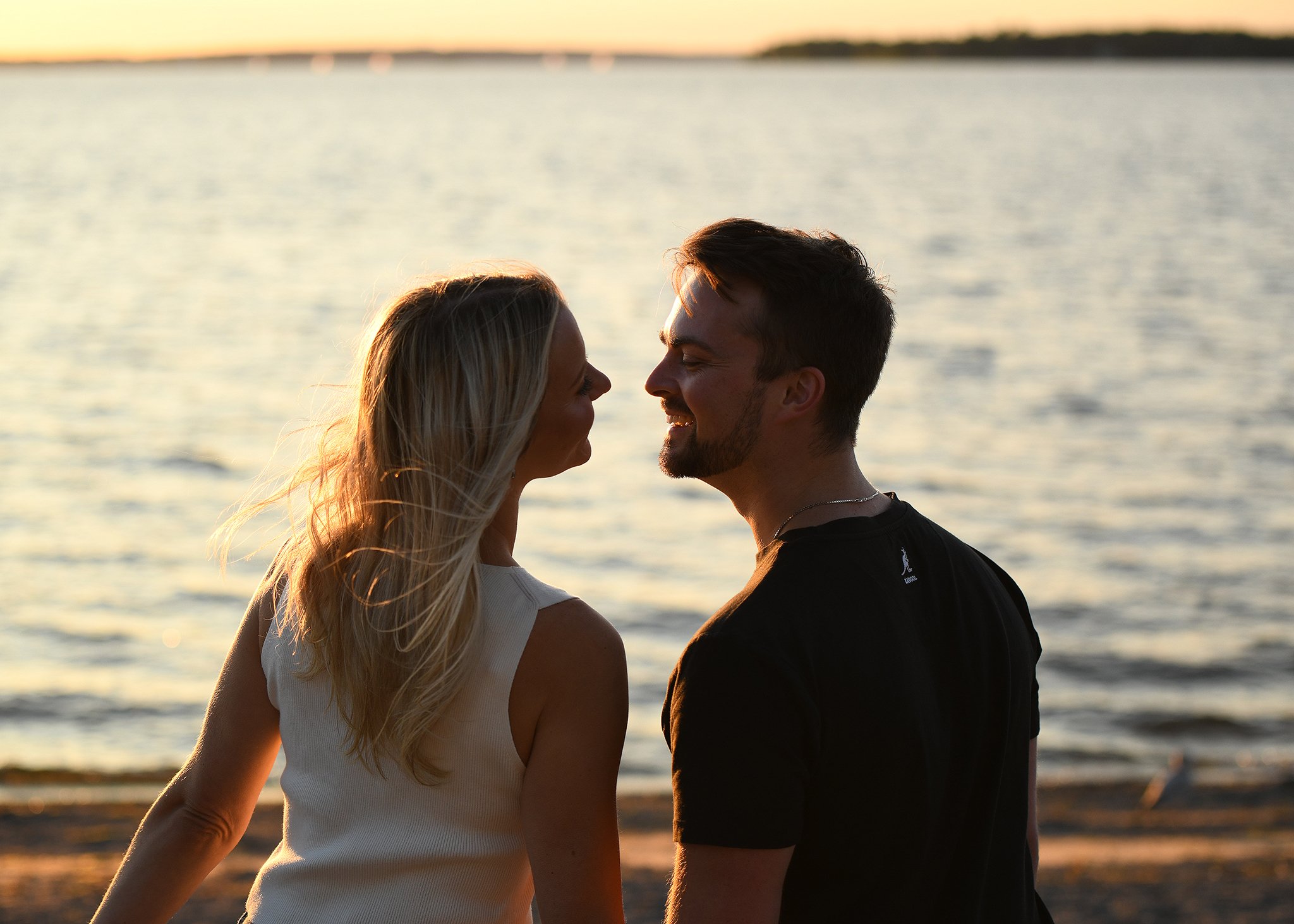 A couple smiling at each other on a beach during sunset.