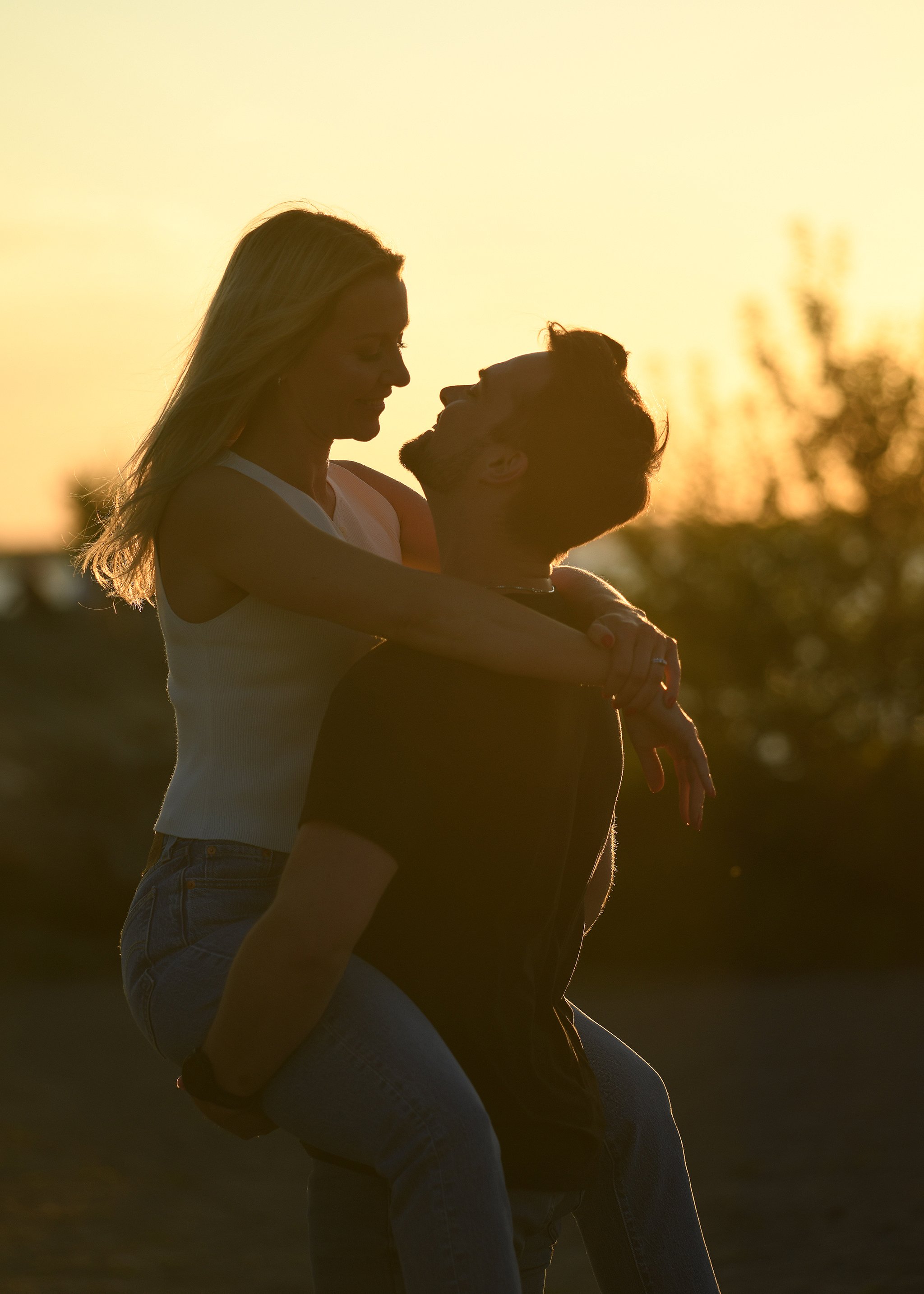 Silhouette of a couple embracing at sunset, woman sitting on the man's lap, surrounded by nature.