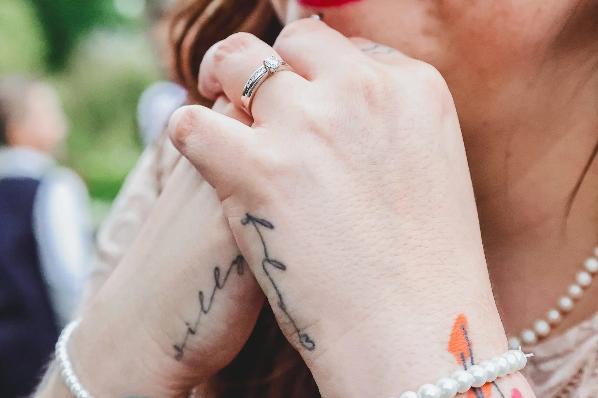 Close-up of a woman's hands with tattoos, wearing a ring and pearl bracelet.