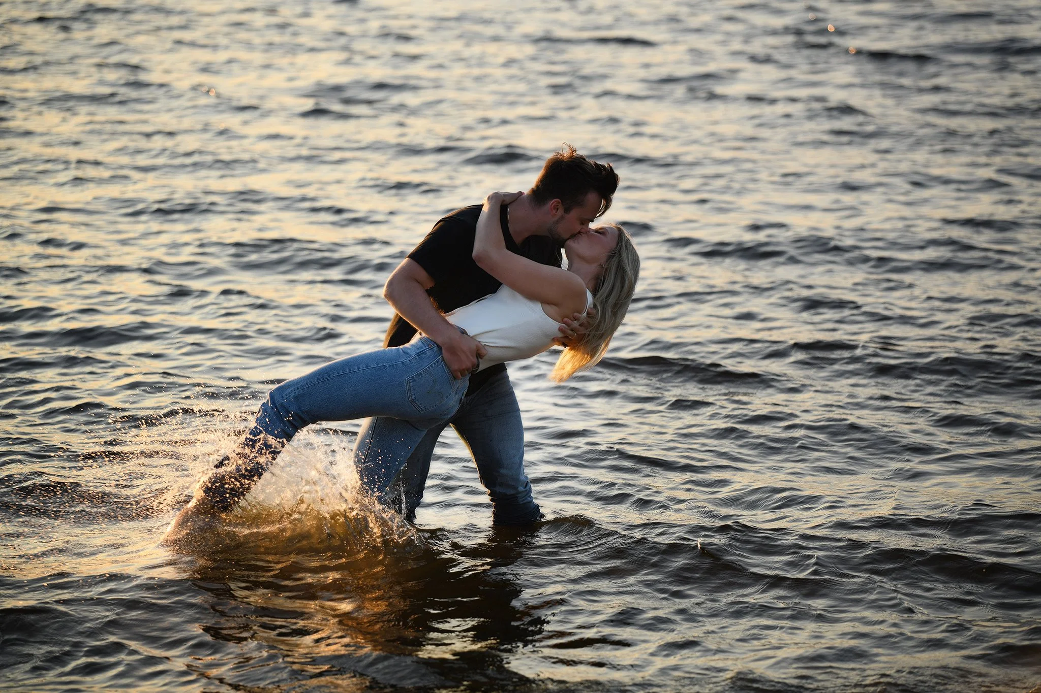 Couple kissing in the ocean at sunset, creating splashes in the water.
