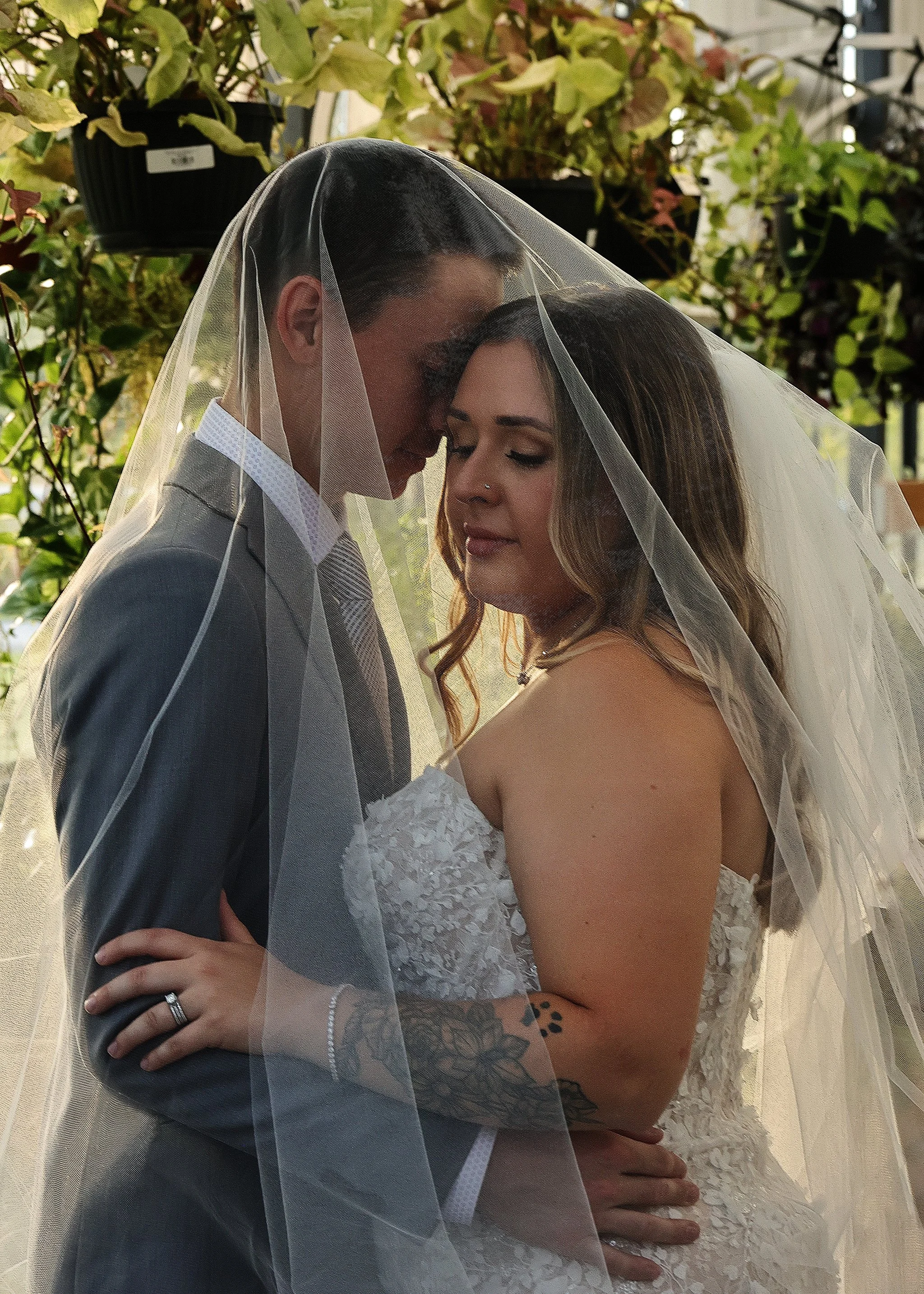 Bride and groom embracing under a wedding veil, surrounded by greenery.