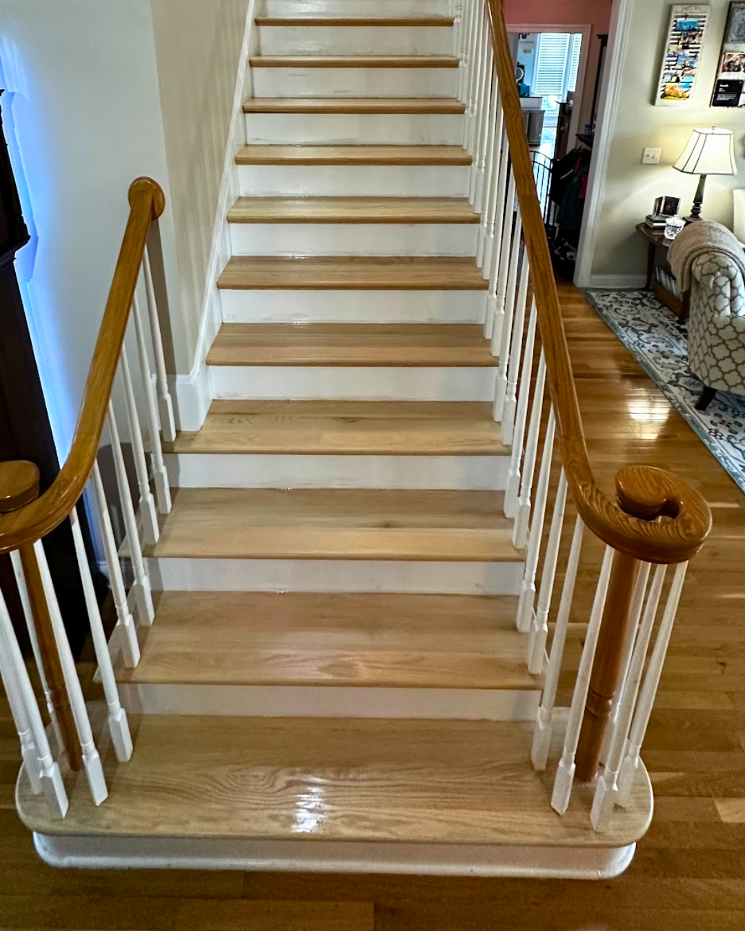 Wooden staircase with white risers and beige treads in a home interior, with a wooden handrail and white balusters on both sides.