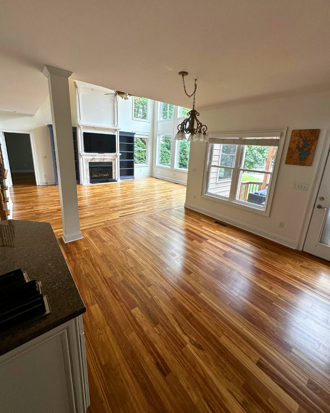 Empty living room with hardwood floors, large windows, a fireplace, and a ceiling light fixture.