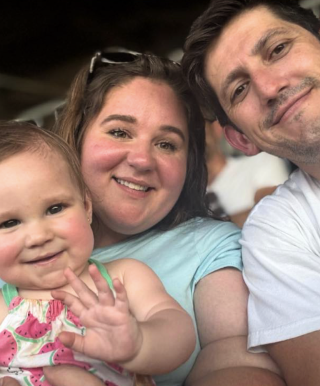 A family of three taking a close-up selfie at a social event, featuring a young girl, a woman, and a man smiling at the camera.