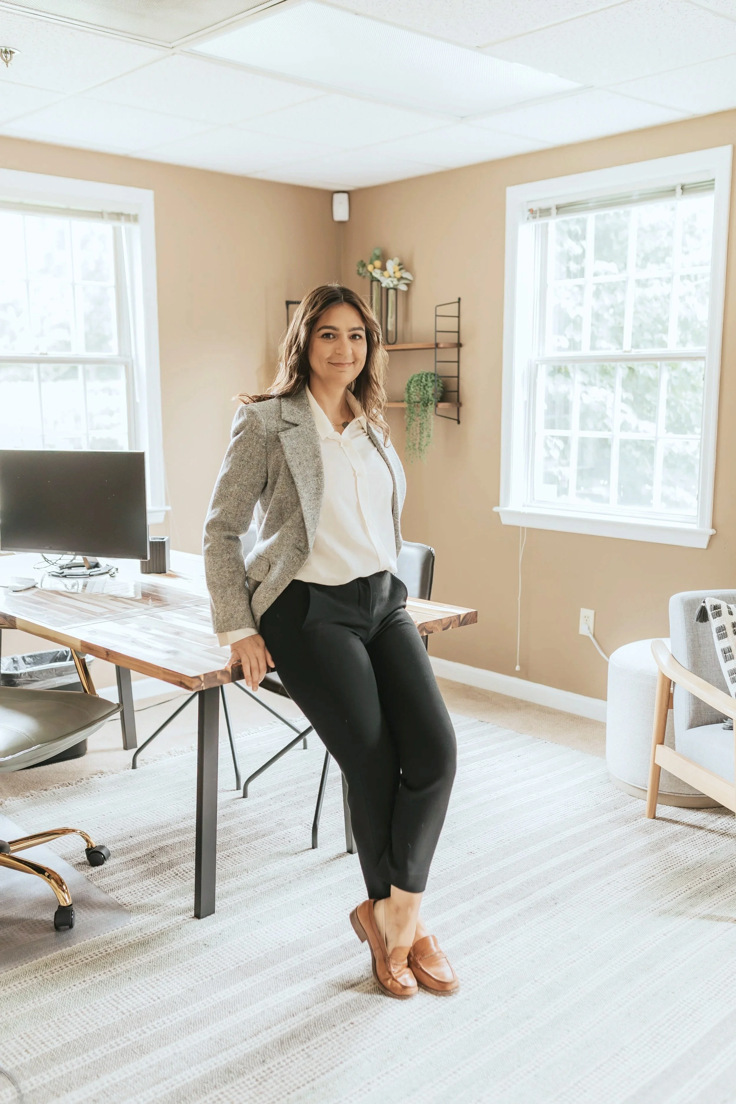 Dr. Graham standing in her office in business attire, leaning on her desk with patient seating and the office's minimalist decor visible.