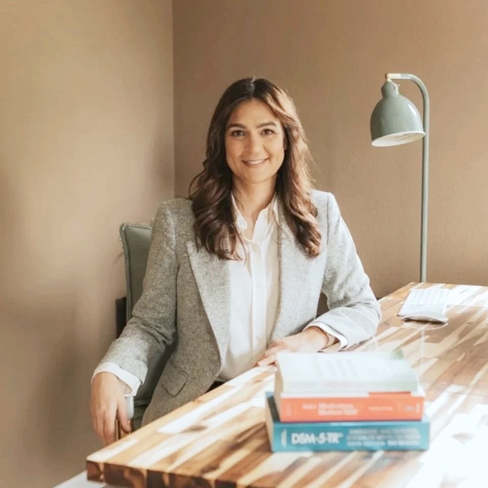 Dr. Graham seated at her wooden desk in her office, wearing a blazer and smiling at the camera.
