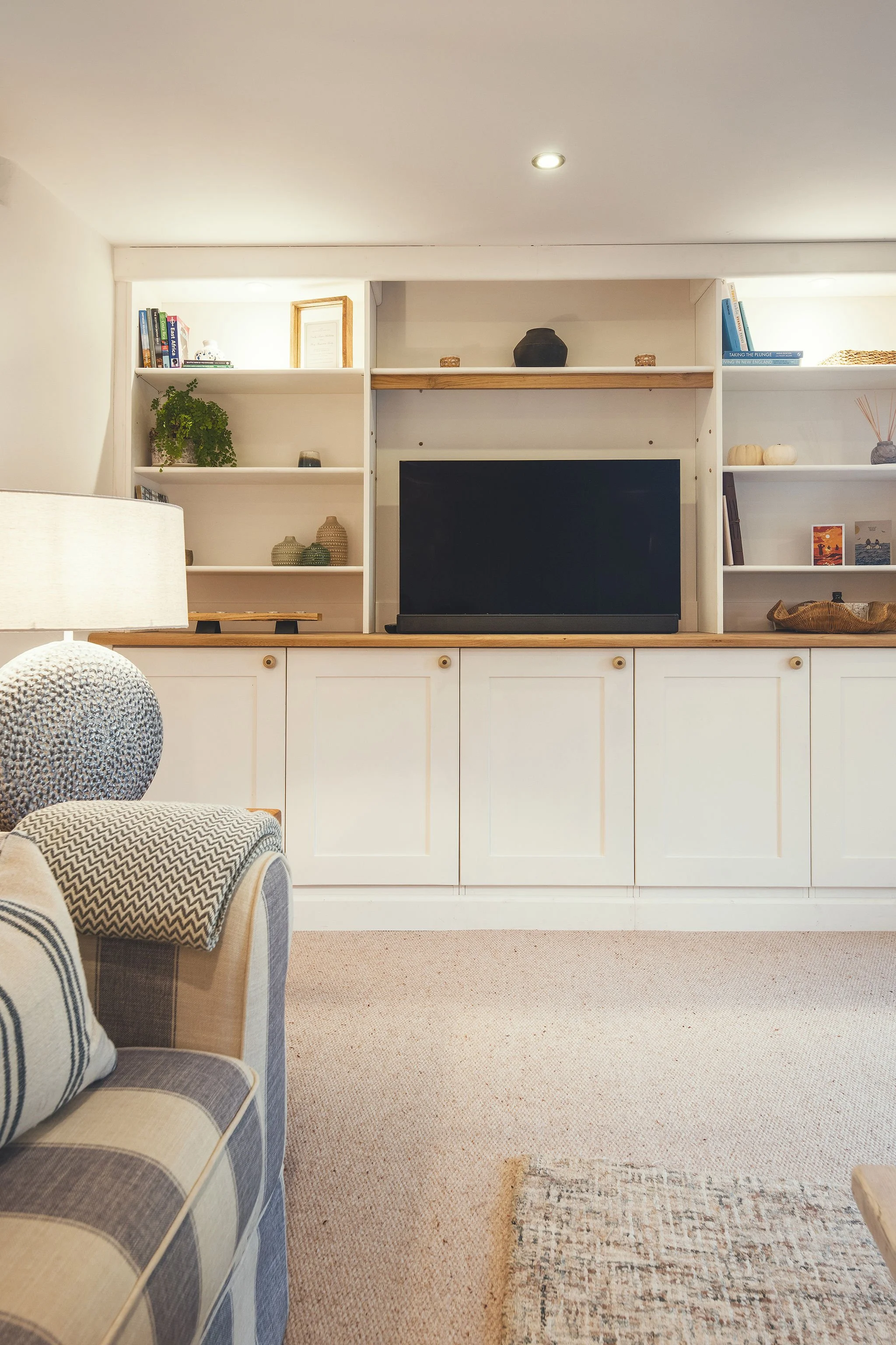 Living room with a white built-in shelf and cabinet, a black TV in the center, and decorative objects such as vases, books, and small artworks displayed on the shelves.