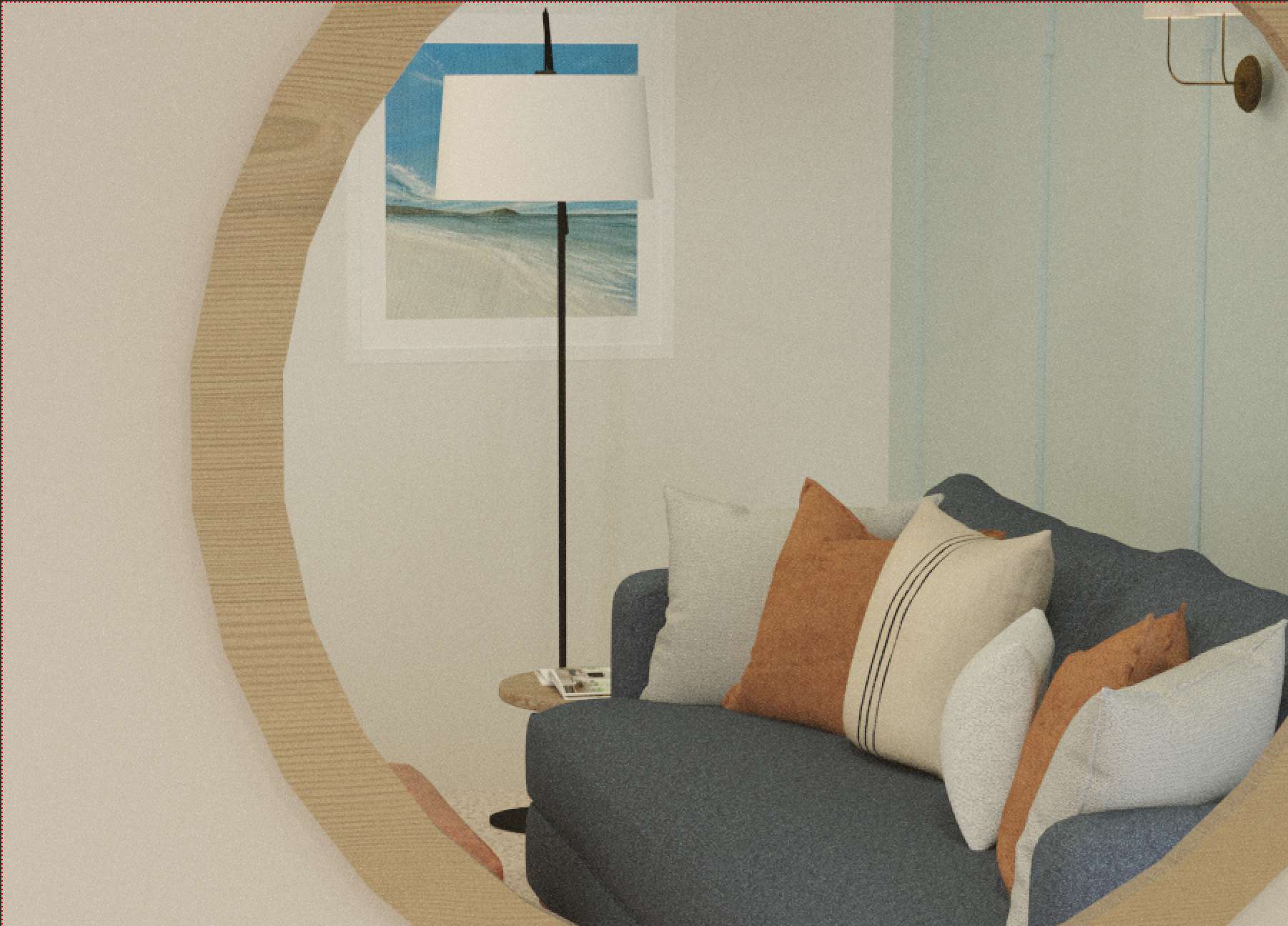 Interior view of a living room with a navy blue sofa, multiple pillows, a round side table with magazines, a tall floor lamp, a beach-themed picture on the wall, and a light-colored wall.