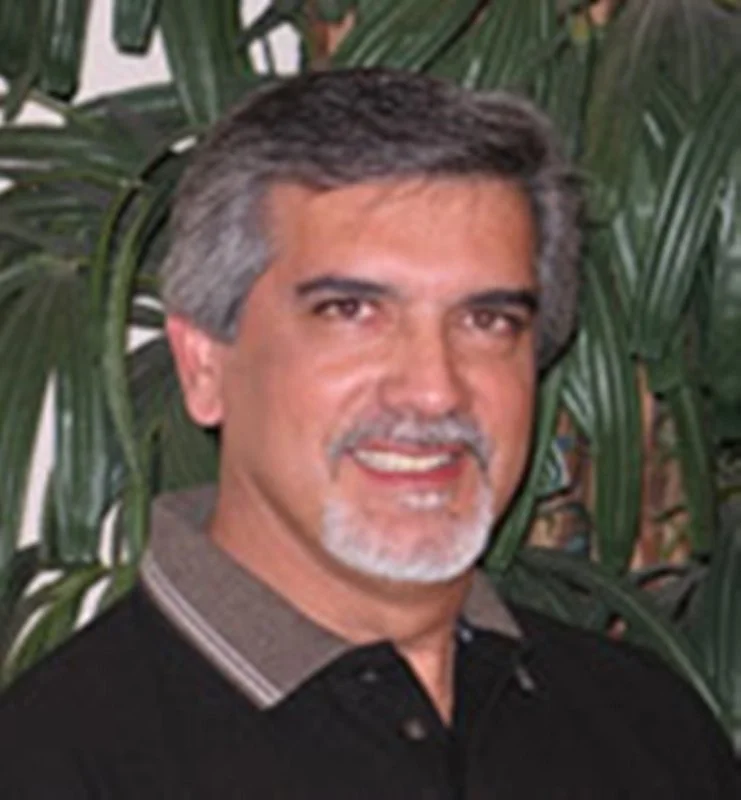 A blurry picture of a man with gray hair against a plant background.