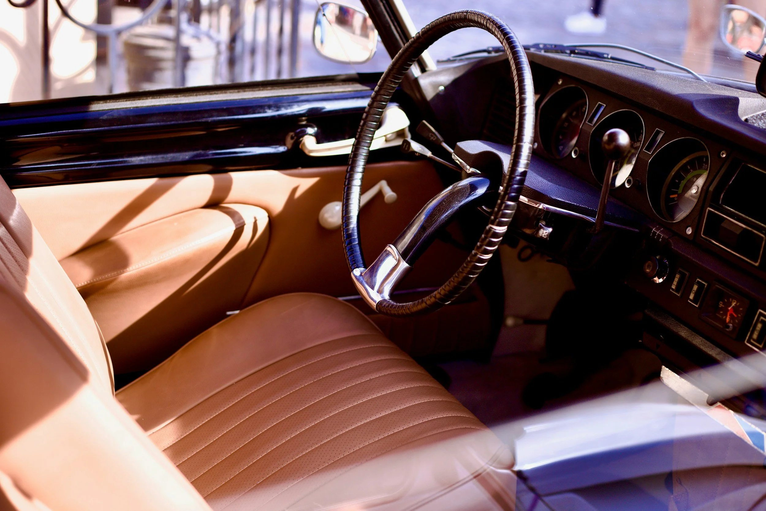 Interior of a vintage car with tan leather seats, a black steering wheel, and a dashboard with gauges and controls.