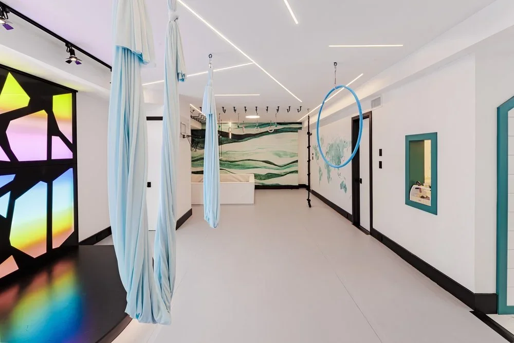 Empty indoor fitness or yoga studio with aerial silks, hula hoop, and gymnastics rings, modern lighting, and colorful murals.