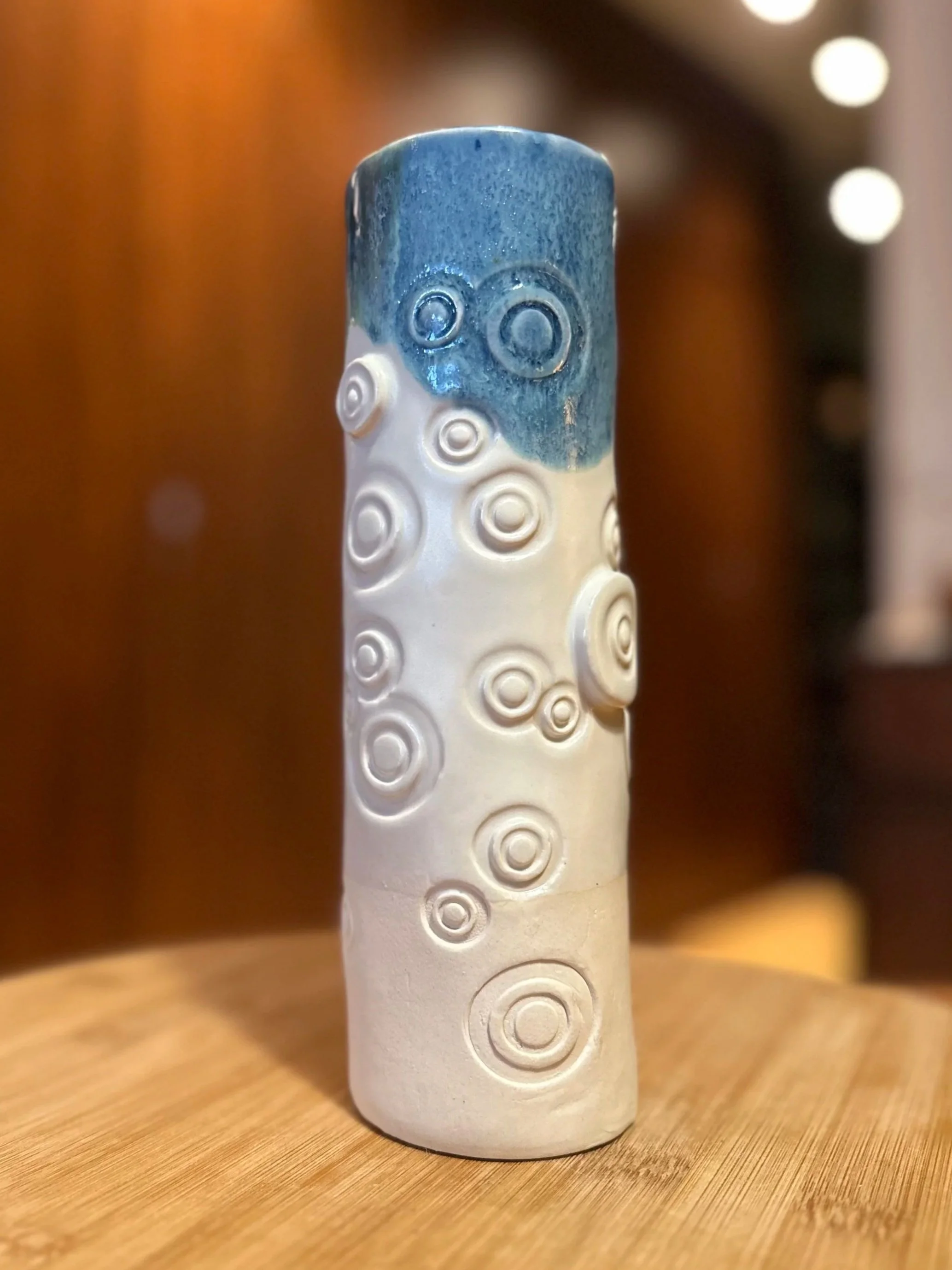 A ceramic vase with a textured surface, painted in shades of blue and white, featuring circular patterns and concentric rings.